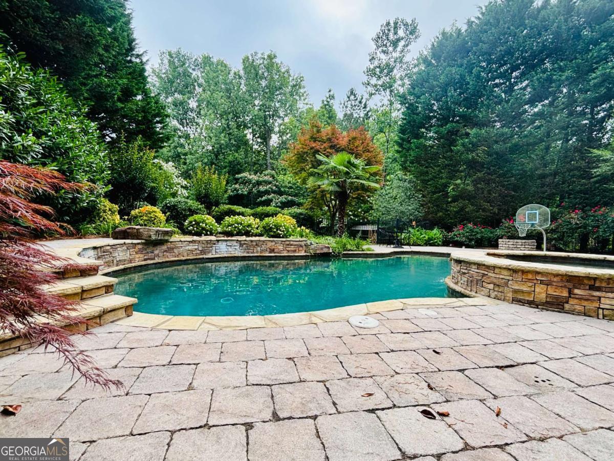 Elegant 4 bedroom, 4.5 bathroom home, 3 sides brick and a 3 car garage, on a beautifully landscaped lot spanning over half an acre in the highly sought-after Olde Heritage swim/tennis community. Ideally located just minutes from Downtown Woodstock, Milton, and Alpharetta, this spacious residence is designed to offer comfortable living and a private retreat. A charming brick-paved rocking chair front porch welcomes you into a two-story foyer and main level boasting hardwood floors, formal dining with trey ceiling, formal living room, and a unique study hidden behind bookshelf doors that opens to a private deck overlooking the pool. The great room features a fireplace and a wall of picture windows, flowing seamlessly into a bright breakfast room and a well-appointed kitchen with granite countertops, stainless steel appliances, ample cabinetry, and access to a large deck. Upstairs, the expansive primary suite includes a sitting area, its own deck, walk-in closet, and a spa-inspired bath with soaking tub, dual vanities, and separate shower. A second ensuite bedroom and two additional bedrooms with shared bath complete the upper level. The finished terrace level adds potential for a fifth bedroom, and boasts a flex room, full bath, family room, and storage, ideal for guests, teens, or multigenerational living. Step outside to your private backyard oasis featuring a sparkling pool with hot tub section, stone pavers, fire pit, fenced yard, and covered outdoor kitchen prep area perfect for year-round entertaining. The three-car side-entry garage includes a Tesla charger. Don't miss this rare opportunity to enjoy lifestyle, space, and location in one of Woodstock's most desirable neighborhoods.