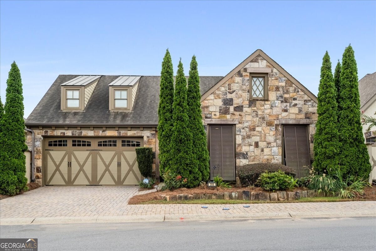 Welcome to this stunning European-inspired home in the gated community of The Village at Towne Lake. With a charming stone front and Bermuda shutters, this residence offers true one level living with no carpet and full handicap accessibility. Inside, the home boasts four spacious bedrooms and two and a half baths, all designed for both comfort and style. The open concept layout features a defined great room with a cozy gas log fireplace, a dining area with an elegant coffered ceiling, and a huge designer kitchen complete with an oversized island, gas range, built-in microwave, white cabinetry, and granite countertops. The primary suite offers ample space, including a sitting area, a luxurious bathroom with zero-entry shower, dual vanities, and an oversized walk-in closet. Both full bathrooms are fully wheelchair accessible. A dedicated office space sits conveniently off the kitchen, while the separate laundry room with sink adds everyday functionality. Additional highlights include: Reverse osmosis water system Two-car garage with an innovative attic elevator lift system for effortless storage access Screened porch leading to a private courtyard with a soothing water feature and retractable electric awning. Community amenities elevate the lifestyle even further with a pool, pickleball courts, and a grand clubhouse featuring a pool table, game area, kitchen, and abundant space for social events. Residents enjoy an active community with clubs, gatherings, and game nights.Perfectly located just minutes from top-rated schools, the interstate, and the vibrant charm of downtown Woodstock.