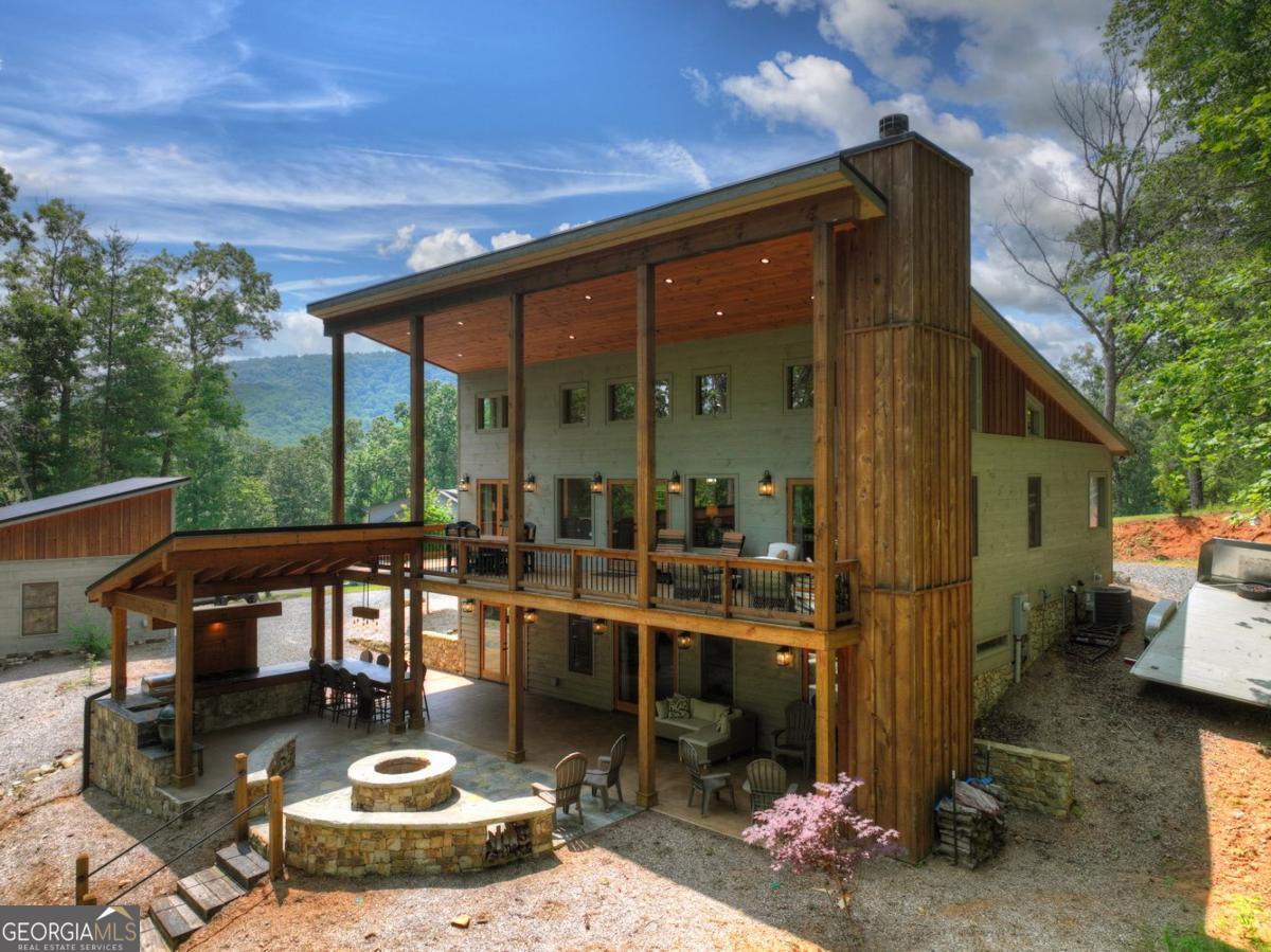 This beautifully designed 4 bedroom, 4 bathroom modern-style home offers luxury living with thoughtful details throughout. The main floor features vaulted ceilings, an open layout, custom cabinetry with granite countertops, and a cozy gas fireplace. Two bedrooms on the main level include private ensuite baths and direct access to the expansive back porch. The terrace level includes two additional bedrooms, each with ensuite baths, a wet bar, and ample storage space. Outside, enjoy professionally landscaped grounds and year-round mountain views that transform beautifully with the seasons. A newly added oversized two-car garage includes a deck and RV hookup for added functionality. The standout outdoor kitchen is fully equipped with granite countertops, a Big Green Egg, cooktop, grill, bar seating, and a grand wood-burning fire pit at the center of it all! This home seamlessly blends modern comfort with mountain charm, offering an exceptional opportunity for full-time living or a high-end retreat! Perfectly situated in a prime location, this property is just minutes from some of the area's best outdoor recreation-enjoy easy access to hiking trails, the Toccoa River, and Lake Blue Ridge!