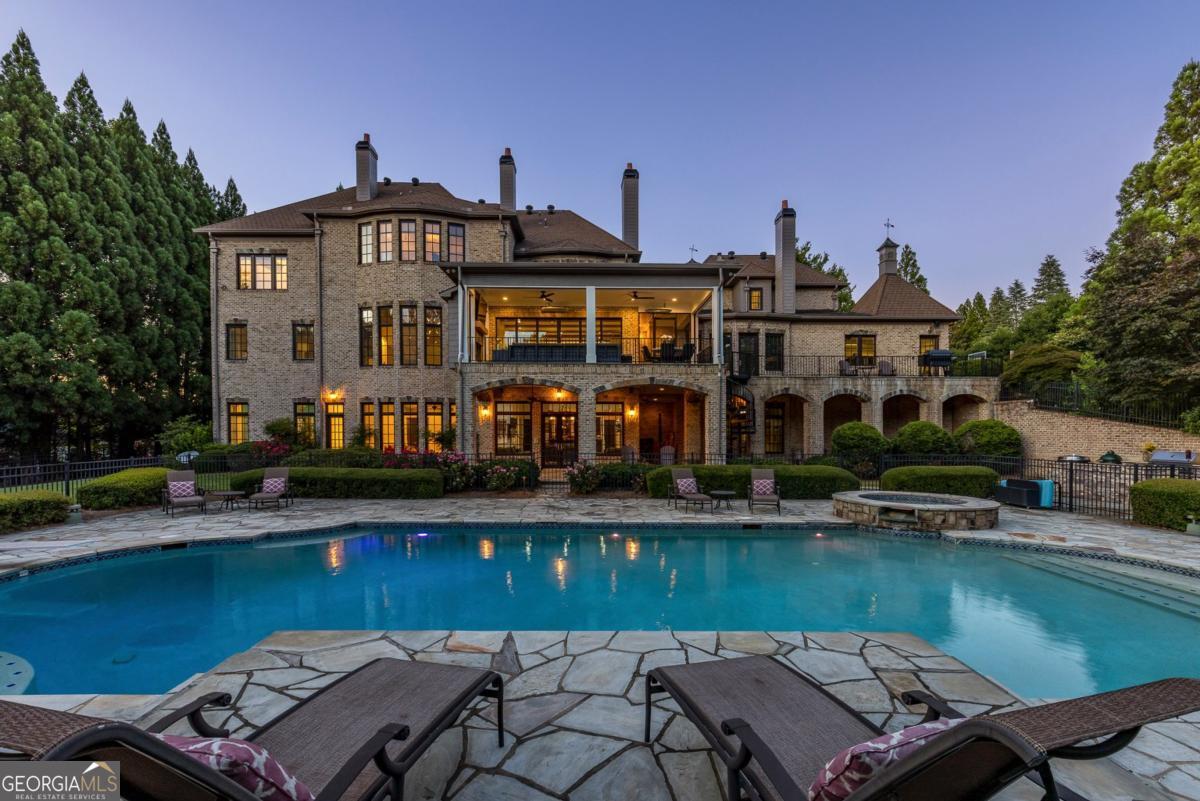 An extraordinary renovation in Johns Creek. Tucked away on a beautifully landscaped, 2.75-acre private lot, this spectacular estate has been completely reimagined by Barbara Dawes Designs, blending timeless architecture with bold, bespoke finishes and curated luxury at every turn. A grand two-story foyer welcomes you with a sweeping curved staircase adorned with iron railing, setting the tone for the artistry within. The formal dining room is anchored by a one-of-a-kind Alex Turco art installation titled "The World is Yours," creating a conversation-starting centerpiece. The fireside family room offers architectural elegance with a coffered ceiling and a striking custom black leather marble mantel. A floating staircase adds to the home's contemporary sophistication. Designed for chefs and entertainers alike, the kitchen is exceptional-featuring a custom pizza oven with artisan tile surround, a large island with quartzite countertops and farmhouse sink, and illuminated glass-front cabinetry showcasing your finest glassware. The culinary experience is elevated by top-tier appliances: a Wolf six-eye range with griddle and retractable Alex Turco backsplash, built-in SubZero refrigerator with dual freezer drawers, SubZero wine refrigerator, and Cove dishwasher. The adjacent scullery kitchen is equally outfitted with a True full-size refrigerator and freezer, Wolf cooktop with wok accessory, Wolf steam oven and warming drawer, Miele coffee system, Sharp microwave, second Cove dishwasher, craft paper dispenser, and custom walk-in pantry. Casual dining flows into a fireside breakfast area and into the keeping room, where NanaWall aluminum folding doors open to an exquisite three-season porch. This seamless indoor-outdoor connection features Bluestone flooring, fireplace, two Bromic outdoor heaters, and fully motorized vinyl shades and screens-creating the perfect year-round gathering space. Thoughtfully designed for everyday living, the main floor also includes a richly appointed library with built-in cabinetry and coffered ceiling, a fully custom mudroom with lockers, bench storage, and built-in planning desk. A dedicated dog room includes raised bathing area, pot filler, and built-in bowls. A spacious laundry room offers two sets of washers and dryers, floating shelves, custom cabinetry, and a farmhouse sink. A serene guest suite on the main level offers a luxurious retreat with Venetian plaster walls, a morning bar with beverage refrigerator, gas fireplace, and a spa-like bath clad in imported Carrara marble. The oversized open shower features dual rain heads and a soaking tub, complemented by a floating double vanity. Upstairs, the fireside primary suite is a true sanctuary with a private sitting area, morning bar, and lavish bath including heated floors, steam shower, soaking tub, dual vanities, two private water closets, and a vast custom closet. A flexible bonus room makes an ideal nursery, studio, or dressing space. Four additional en suite bedrooms are generously sized, each with custom finishes and elegant bathrooms. The finished terrace level extends the home's luxury with a fireside media and lounge area, full bar, game room, exercise room, guest powder room, and spa bath with sauna, steam shower, and pool access. A secondary laundry room makes entertaining poolside effortless. Outdoors, enjoy resort-style living with a custom pool and spa, surrounded by a fully equipped outdoor kitchen including a built-in Evo gas grill, Eco flat-top griddle, Green Egg, and beverage cooler. A large, level grassy yard offers ample space for play, gardening, or entertaining. Every detail has been carefully considered-from brand-new 5/8" wire-brushed engineered hardwood flooring and wood beams to seven fireplaces and unparalleled finishes throughout. A rare offering blending craftsmanship, comfort, and designer flair in one of the most desirable and private settings.