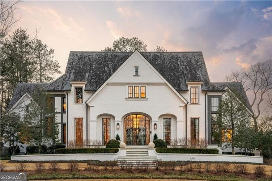 A triumph of architectural refinement, this distinguished estate, designed by the esteemed Linda MacArthur, constructed by the renowned Ladisic Fine Homes and exquisitely appointed by interior designer Brian Watford, exemplifies the seamless integration of classical proportion and contemporary sophistication. Inspired by an English country estate, the residence is a study in craftsmanship, where every detail exudes a commitment to quality, scale and integrity. The residence features a U-shaped layout that wraps around a beautifully landscaped backyard and pool, fostering a connection between indoor and outdoor spaces. Beyond stately steel doors, an intimate foyer unfolds with groin-vaulted ceilings and stone flooring, showcasing the home's architectural precision. The formal living room is a composition of restraint and refinement, with curved walls, lacquered ceilings and steel-framed doors opening to manicured grounds. Adjacent, the dining room commands attention with a herringbone wood-inlay ceiling. The home office features elegant steel doors, custom built-ins and floor-to-ceiling windows. At the heart of the residence, the family room features beamed ceilings, a custom fireplace and wood-wrapped cased openings, creating a sense of warmth. The kitchen, conceived for both culinary artistry and visual impact, boasts waterfall stone counters, an oversized steel-framed window and Wolf appliances, including a professional range and double ovens. A hidden scullery with a prep sink, ice maker and double appliance garages ensures effortless entertaining and discreet functionality. The adjacent bar room, enveloped in high-gloss lacquered millwork, houses an ice maker, dishwasher and beverage and wine refrigerators, exhibiting a commitment to elevated hospitality. The main-level primary suite includes a sitting area, dual couture dressing rooms and a marble-clad bathroom featuring heated floors, dual water closets, a steam shower and a makeup vanity. A floating staircase with a custom iron railing ascends beneath a three-story bespoke lighting installation. Ascending to the upper level, three large ensuite bedrooms flank a bonus room outfitted with integrated surround sound. A fitness suite with a full bathroom completes the usptairs. The lower level is an ode to conviviality, where brick herringbone floors and polished concrete set a counterpoint to the home's refined upper levels. A full bar presides over a billiard room, an open-concept media salon with a projector and reclaimed wood wall and a cocktail lounge swathed in upholstered paneling. A temperature-controlled wine cellar and powder room complete the lower level. The residence is fully integrated with Crestron smart home automation, affording control over audio, climate and security. Corner-set fenestration on all three levels ensures an interplay of light and shadow. Beyond the incomparable interior, the property's meticulously curated exterior features a resort-caliber pool, a covered loggia featuring a wood-inlay ceiling, built-in heaters and an outdoor fireplace, integrating with a professional-grade outdoor kitchen. A separately fenced dog run and a dedicated indoor/outdoor dog room offer dog-tailored accommodations. Every aspect of this estate has been executed at the highest level, ensuring a residence of rare distinction and enduring relevance at the base of Kennesaw Mountain, and in close proximity to myriad shopping and dining opportunities in the heart of Historic Marietta.