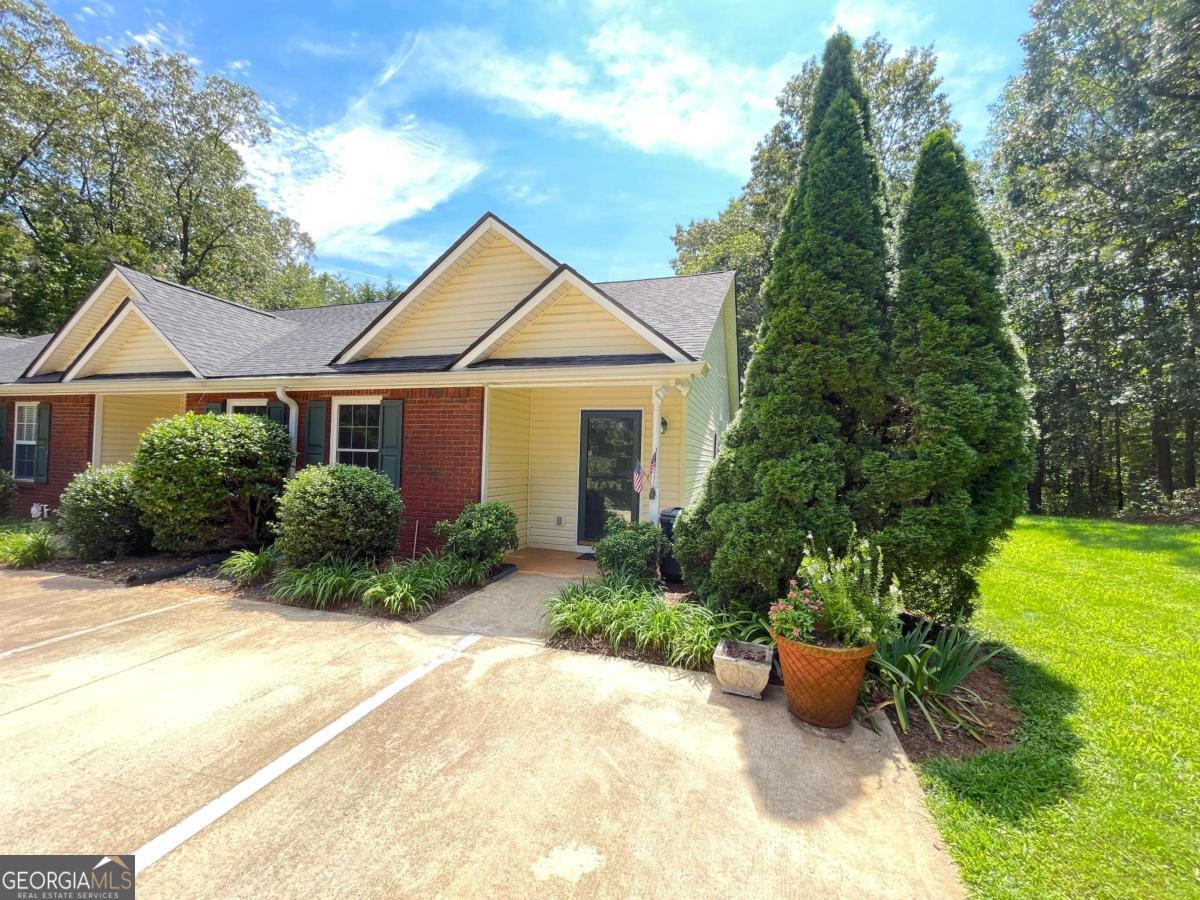 Fabulous End Unit Condo in Hidden Hollow. True to its name, this one is one of the most private, serene and wooded communities in North Hall. Enjoy the private back yard from the spacious patio with its well manicured and beautiful landscaping. Covered front porch opens into a nice foyer, open concept great room, dining and kitchen. Split bedroom floor plan with each having access to private bath. Primary bedroom suite faces the rear, huge walk in closet and walk in shower. Front bedroom is huge, private access to full bath, walk in closet and additional double wide closet. Kitchen with granite countertops tile floors and laundry room equipped with cabinets and shelving. This home has tons of storage with four closets, pull down attic stairs leading to floored space for even more storage, and back patio has a garden shed. Another nice bonus is the unit has three assigned parking places and mail box is on the property. HOA covers water, septic, exterior landscaping and structure maintenance, including driveway, roof, gutters, exterior doors and windows, patios and porches and exterior insurance for the home.