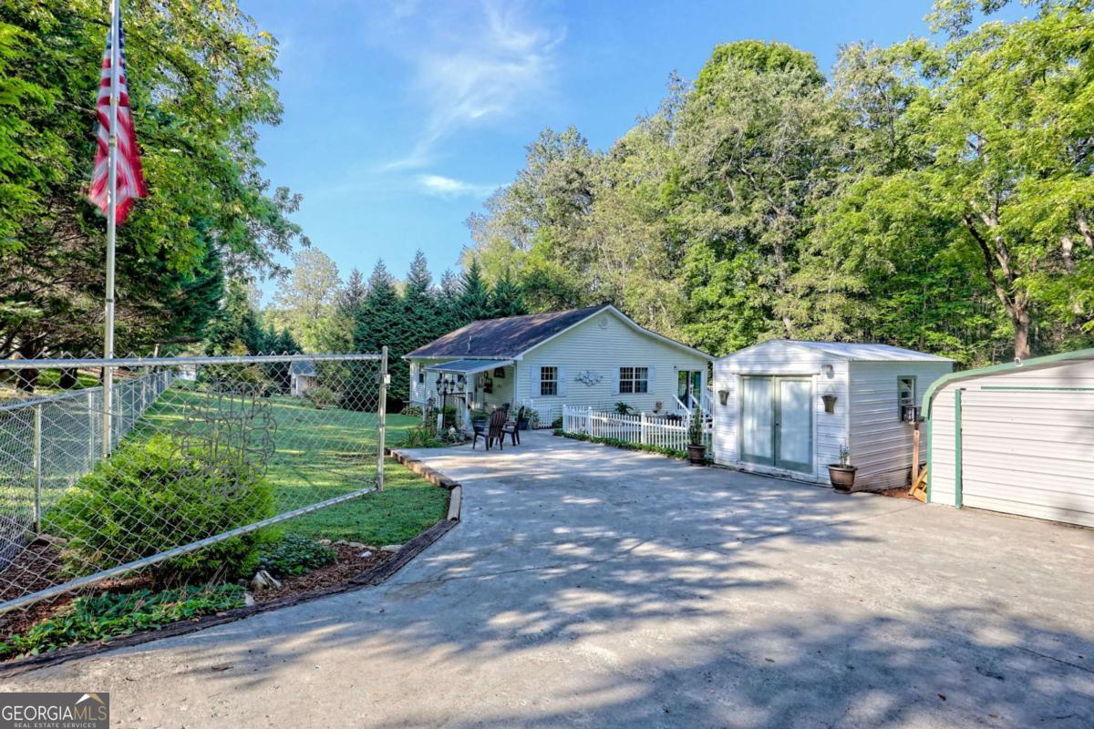 Charming cottage offers one-level living with 2 bedrooms and 2 bathrooms. The updated kitchen is equipped with new stainless-steel appliances and features a built-in bar with a butcher block countertop and convenient seating, seamlessly connecting the dining area to the living room. Relax in the cozy sunroom, which is complete with a gas log fireplace. The outdoor space is a gardener's paradise, with established garden areas enclosed by white picket fences. The fenced yard, featuring a gated entrance, provides security and ample space for outdoor activities on this private 61-acre lot. The rear boundary of the property is the babbling brook. Storage is plentiful, as there is a small workshop with power and a detached 2-car metal garage with 50-amp service. Recent renovations include updated flooring in the kitchen and bathrooms, new faucets and toilets, freshly painted cabinetry, and a spacious 16x26 deck overlooking the yard. Conveniently located across from Lake Chatuge and approximately 3 miles from Hayesville, this home offers comfort and privacy without an HOA, along with nearby conveniences.