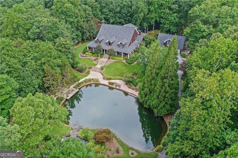 MOTIVATED SELLERS! This home is priced to SELL!! This stately 5-bedroom home, nestled on 4.39 acres of picturesque land along the serene shores of Lake Lanier, offers the perfect blend of privacy, luxury and tranquility. With breathtaking views of the water and surrounding nature from the wraparound porch, this expansive estate features a grand indoor pool with an attached spa, ideal for year-round enjoyment and relaxation. The beautifully landscaped grounds boast a charming pond, waterfall, and a peaceful walking trail that winds through the property, are perfect for enjoying the natural beauty of the area. A private dock provides direct access to the lake, perfect for boating, fishing, or simply relaxing by the water. The primary bedroom suite is a true retreat, featuring a cozy fireplace, a large bath with a double shower that is stubbed to transition to a steam shower, and a private entrance directly to the pool-providing the ultimate in comfort and convenience. The two upper-floor bedrooms share two well-appointed Jack-and-Jill bathrooms with stunning pond and lake views, offering both privacy and beauty. In addition to the main residence, the property includes a spacious carriage house with a 3-car garage, bath, kitchen, and living/sleeping area-providing the perfect space for guests, extended family, or as a private retreat. Could also be used as a short-term or long-term rental. Same waterway as FishTales/Hideaway Bay, and PigTales, and Twisted Oar are just a quick boat ride away. Water at dock is 12'