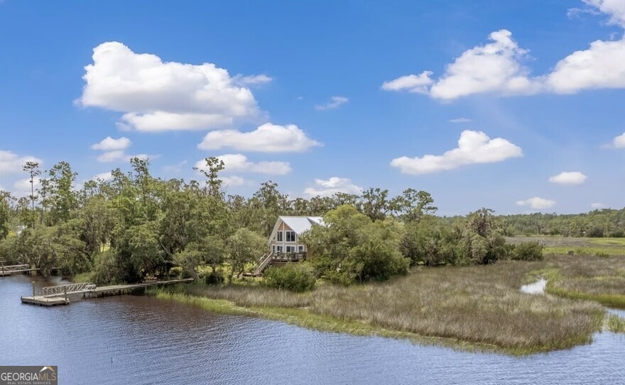 Discover coastal living at its finest with this 3 bedroom, 2 bathroom home perched along the tidal South Newport River. Nestled at the end of a quaint neighborhood peninsula, this property offers unmatched privacy with water on two sides, sweeping marsh and ocean views, and your very own private dock at the river's mouth. The home sits among majestic oak trees and feels wonderfully secluded-yet you're only 5 minutes from I-95 and conveniently located between Savannah and Brunswick. Nature lovers will enjoy frequent deer sightings, landscaped grounds, and tranquil surroundings that feel worlds away. Inside, you'll find thoughtful updates including a new metal roof, new carpet, fresh paint, and new kitchen appliances. Fiber optic internet is installed, and the home includes Generac generator system-capable of powering the entire home for up to 10 days. Additional features include a raised foundation with brand-new storage underneath, a cinder block walk-in tornado/emergency shelter, and a large front deck plus side porch perfect for taking in the views. The upstairs master suite includes an office nook and oversized walk-in closet. The living room showcases breathtaking water and marsh vistas, while the open design allows you to fully enjoy the natural setting. This sale also includes an additional .55-acre lot (Tract 2), providing even more room and value. Whether you're seeking a full-time residence, a peaceful retreat, or a nature-lover's getaway, this property offers the rare balance of seclusion, beauty, and convenience.