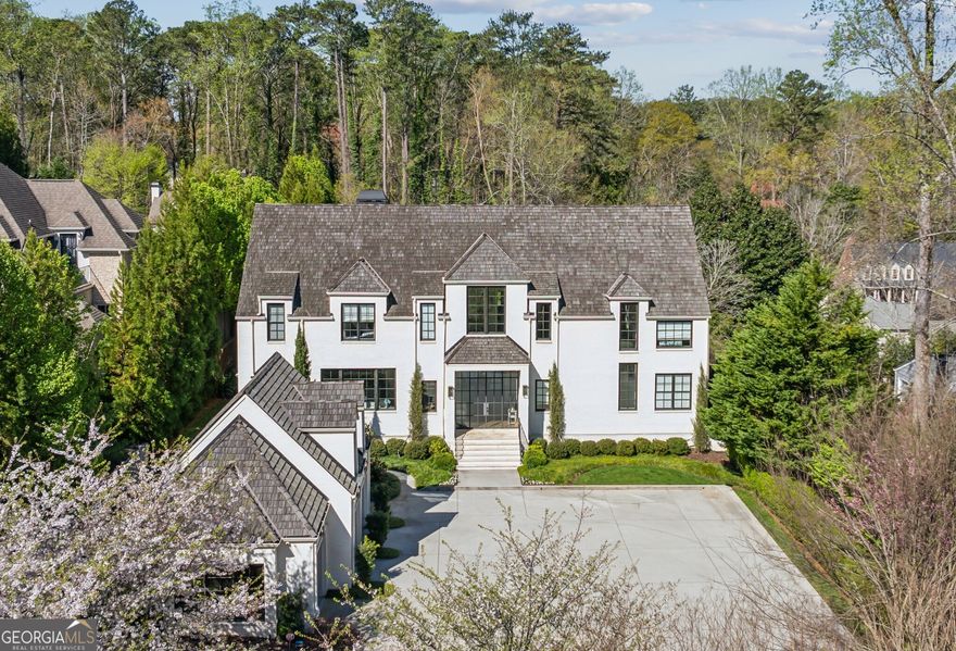 Tucked within a landscape of understated splendor lies a home that feels conjured from the pages of an architectural fairytale - a place where timeless design and modern luxury meet in perfect harmony.  Beyond its gracious fa ade, through arched entryways and steel-framed doors, the home invites you into a world curated with natural stone, warm wood, and whispers of elegance at every turn. Each corner reveals an artisan's touch - a celebration of craftsmanship and refinement.  The main level unfolds like a grand but welcoming salon: soaring 12-foot ceilings stretch above herringbone-laid hardwoods, as rooms ebb and flow with a rhythm made for both everyday comfort and effortless entertaining.  To one side, is the formal living room, a wonderful space to sit and enjoy the natural sunlight that pours through the floor to ceiling windows. On the other side is the heart of the home, the chef's kitchen crafted for both form and function - a symphony of bespoke cabinetry, not one but two oversized islands, dual dishwashers, and the gleam of Wolf and Sub-Zero appliances. A dramatic range hood crowns the space like a modern-day sculpture, while marble countertops glisten under soft morning light. A cozy keeping room nestles near the hearth, inviting intimate gatherings and unhurried mornings. And yes - a wet bar awaits with an ice maker, wine refrigeration, and the promise of perfectly chilled pours.  On this same level, a private guest suite offers a haven for overnight visitors, thoughtfully tucked for comfort and ease. Nearby, a mudroom stands ready to catch the day's comings and goings with understated style.   Ascend the staircase to discover the sanctuary that is the primary suite - a world of its own, complete with a  fireplace, morning bar, and spa-like bath. Soak away your day in a sculptural tub, glide between dual vanities, or relax in the glass-enclosed shower that feels more like a boutique spa than a bathroom. Two generous custom closets complete the suite with room to breathe and room to dream.  Four additional bedrooms extend across the upper level - each spacious, sunlit, and connected to exquisitely appointed baths. Each room offers a unique canvas - the perfect suites for a serene nursery, a welcoming guest retreat, or a beautifully tailored space to fit your every desire and whim.  But the home's most unexpected magic awaits on the terrace level - a fully finished destination where play, indulgence, and hospitality converge. Picture a sprawling lounge and media space, anchored by a custom bar that wouldn't feel out of place in a luxury resort. Nearby, a card room glows with the ambiance of a rustic fireplace with tongue-and-groove surround. For connoisseurs, a 1,200-bottle climate-controlled wine cellar stands ready for both storage and story-worthy tastings.  Wellness seekers will adore the private gym, while golf enthusiasts will revel in a high-end simulator that brings the fairway to you - no matter the season.  Outside, the enchantment continues. A saltwater pool and spa shimmer under the sun, framed by sleek stone and surrounded by the sounds of nature. A covered patio invites alfresco feasts with its built-in grill and wood-burning fireplace - a four-season gathering place for laughter, lounging, and long conversations under the stars.  A fully appointed pool house that dazzles: gourmet kitchen, stainless appliances, full bath, laundry, and dramatic 15-foot glass nano doors that fold entirely open to blur the line between indoors and poolside paradise. Here, summer lives all year long. Aside from it being a haven for high end living and entertaining, it is equipped with the finest systems to provide ease day to day.  In every detail, this home whispers luxury - not loudly, but confidently - knowing its beauty lies not just in extravagance, but in its balance of soul, story, and sanctuary. This is more than a residence. This is a life well-lived.