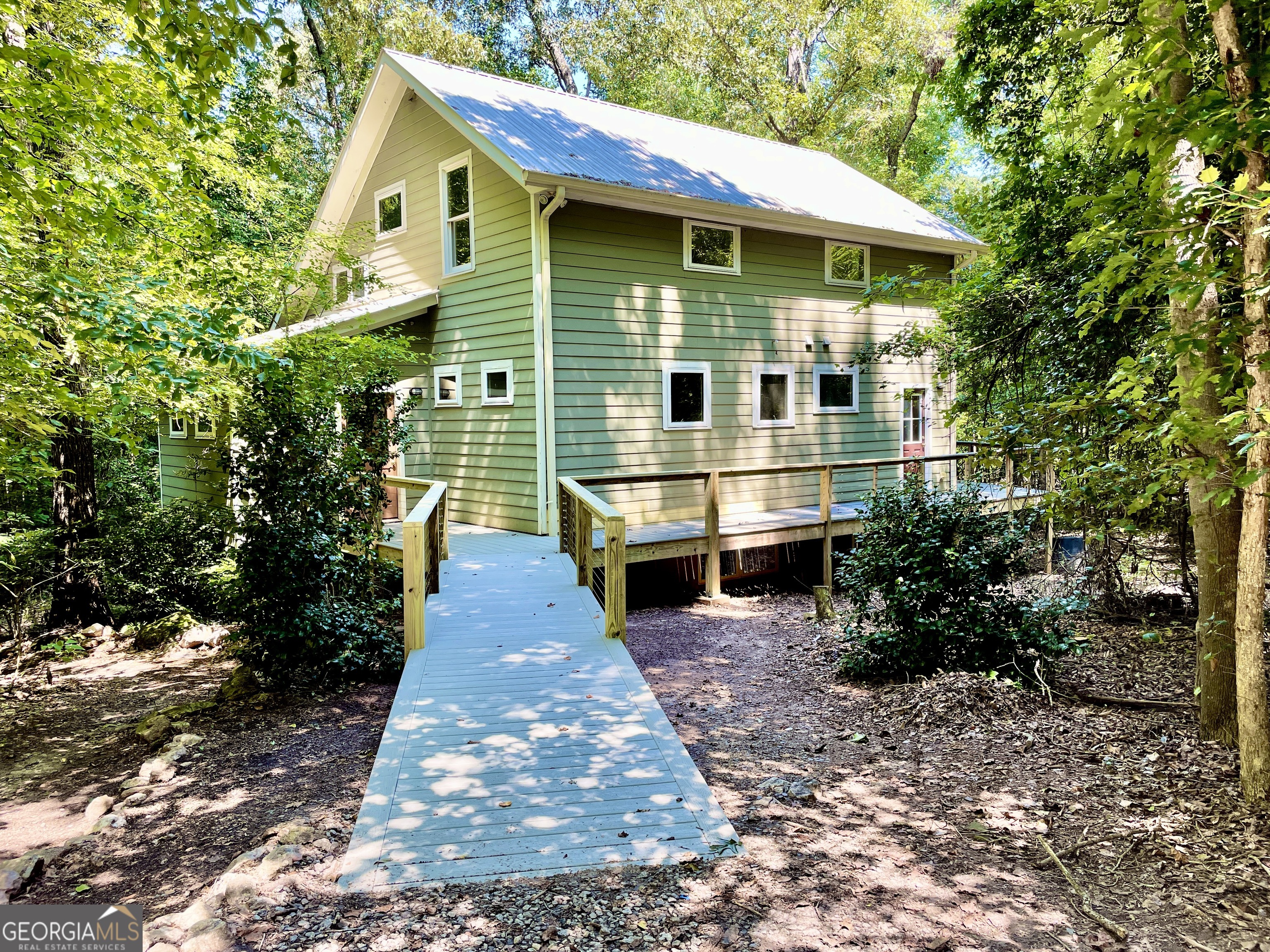 Nature Lover's Dream Home in Kenney Ridge Community. Welcome to 345 Three Oaks Drive in Kenney Ridge, an intentional community designed for birders, hikers, naturalists. While there are no manicured lawns or perfectly trimmed hedges, those seeking a peaceful, nature-centered lifestyle can find it here. It's a close-knit community where neighbors keep in touch with each other, join committees to help out, and remain committed to preserving local wildlife and native plant habitats. This sought-after neighborhood features a community garden, clubhouse offering regular community-wide events and peaceful, wooded trails surrounding the area. Simply step out the back door for direct access to miles of walking trails and more than 50 acres of common land including woods, streams, and meadows. Nestled in the forest, this custom-built home was built with sustainability in mind. It features: two heating zones, Low-E casement windows, extra insulation, and high-efficiency water heater. Handcrafted natural wood doors, trim, and finishes by renowned craftsman George Wright lend character and warmth to every room. A newly built ramp leads to the handicap-accessible main floor. This main-level offers a bright entry hall/mudroom/foyer with a large walk-in storage closet with a window there's a nice coat hanging wall. The kitchen boasts granite countertops, gas cook top, electric oven, stainless steel fridge, and a row of pantries with plenty of storage area. Next to the pantry is the laundry area with room for a stacked washer and dryer and an area for hanging clothes. Main-level primary suite includes two walk-in closets, tiled bath with soaking tub and a separate shower. The great room has large windows and nearby tiled half bath with a bidet. Attractive wood floors and tall built-in shelves for books, art, and collections add to the beauty. Also, it's easy to enjoy outdoor living on the screened-in covered porch, complete with ceiling fan and multiple power outlets. A side deck leads to the front entrance. Upstairs, distinctive square handrails on the staircase add a custom touch. A cozy, open bonus room is by the two bedrooms and tiled bathroom. The fully finished daylight basement includes polished concrete floors, a studio/guest room/office with sink and separate exterior entrance, and spacious living/rec room with a couple of large, walk-in storage closets. In addition, a private bedroom with utility closet (water heater & HVAC) is near the fully tiled bathroom with a bidet. Next to the bedroom, an office/guest room with built-in bookshelves and woodland views is a comfortable, quiet space. This floor offers the option to add a kitchenette making it ideal for an in-law suite or multi-generational living. Additional Features: 4.5+ acre lot, a fully fenced garden area, a storage shed, total privacy in a serene wooded setting only minutes from shopping and downtown Athens, 3 Air Conditioners (one for each floor), both downstairs heaters are gas, heat pump on the 3rd floor. A large, productive fig tree is a beautiful asset in the backyard, too. 345 Three Oaks is ideal for multi-generational families, artists, remote workers, and nature lovers. Look for a variety of birds, insects, bats, snakes, turtles, and butterflies around the house and along the cool trails. At night, neighbors are courteous about not shining bright lights. This allows nighttime skywatchers to enjoy the stars. The sights and sounds of nature abound in Kenney Ridge! If you seek a peaceful, eco-conscious lifestyle in a vibrant, supportive community, this thoughtfully designed, one-of-a-kind home in Kenney Ridge is well worth considering. More info at https://www.kenneyridge.org/. Buyers must agree to follow all HOA rules, Covenants & Restrictions and By-laws, and drive slow. Preferred attorney is Jack Frierson 706 549 4646 jack@friersonlaw.net