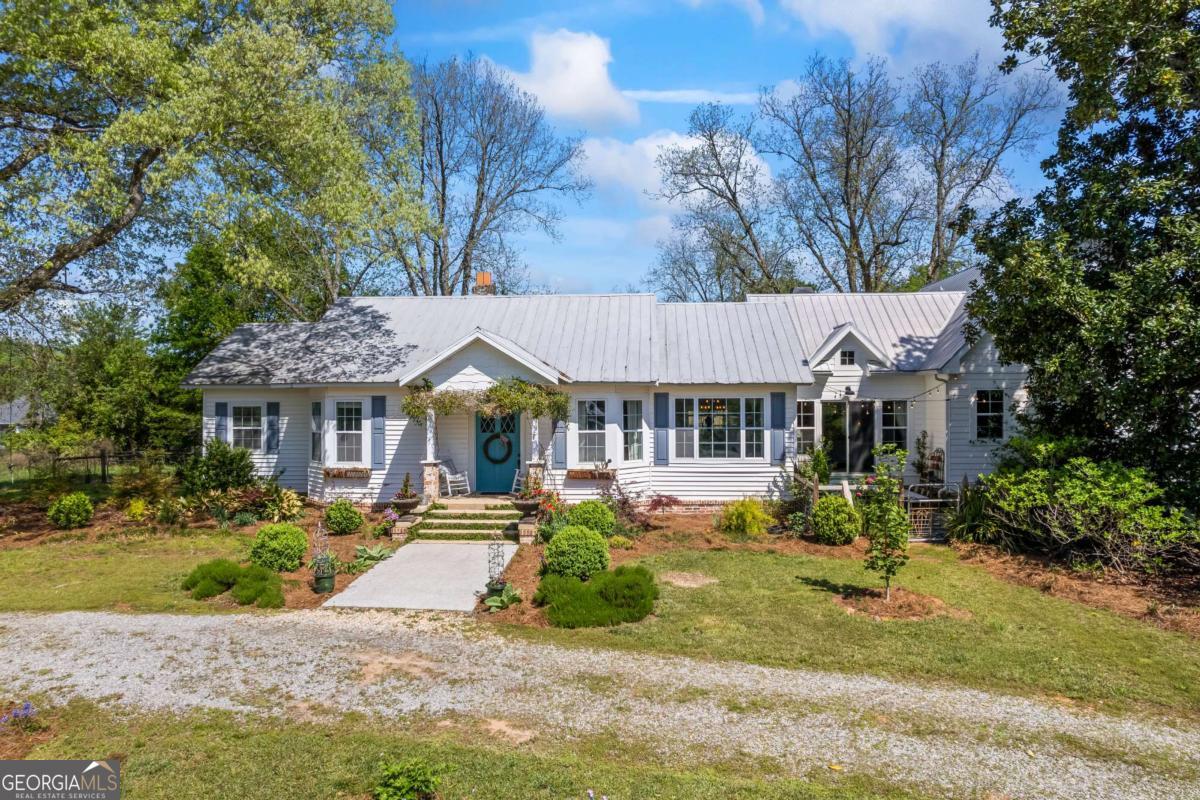 Welcome home to an amazing property on 10 acres in South Oconee County offering flowering shrubs, trees, numerous perennials, grasses and bulbs. Historic plants on the property include pomegranate, pear, newly planted blueberries and thornless black berries. The original home was built in 1910 and the current owners completed an addition in 2020, adding 2220 heated sq. ft, two large porches, barn renovations, fencing/cross fencing of the entire 10 acres. All of the details -the metal roof, the moldings, the large windows providing expansive views of the property allow for bountiful natural light. Original oak hardwoods are in the original part of the home and reclaimed 12" wide 1" thick heart pine flooring is throughout the new entryway off the covered porch, the new Great Room and Kitchen harvested from the second floor of the onsite workshop building. As you enter the original front door from 1910 notice the large diamond pane glass. Three additional diamond pane doorways from a mill in Pennsylvania are in the home as well as a built in cabinet to the left of the front featuring the diamond panes and a new wood door on the right porch that was designed to replicate the original doors. The family room has a fireplace with vented gas logs, triple crown molding, built in shelving with electrical hookup that was originally a picture window that can accommodate a large flatscreen TV. To the left of the family room are three bedrooms with one featuring an original coal burning fireplace that is now decorative and two bathrooms. One bath features a large tiled shower and two separate vanities. The Dining Room has wainscotting and a coffered ceiling. The kitchen was expanded with a new bar top with seating for eight and features a 21 opening into the new family room with vaulted ceilings with beadboard and reclaimed wood beams from the barn. An original barn loft door has been installed above the new brick fireplace. Brick surround was constructed with new and old brick with wavy mortar joints to authentic the look of the old farmhouse. A functioning wood cook stove seated on a brick hearth was installed in the breakfast area. There is a walk-in pantry with one of the diamond paned doorways with slate flooring and space for an additional refrigerator or freezer. A new appliance closet is located adjacent to the pantry. Large sliding glass doors allow views of the courtyard with flagstone paving, flanked with beautiful plants and a historic granite table for outdoor meals and gatherings. Outside the great room is a new screened porch with vaulted ceilings, 5V metal reclaimed from the home addition as and wood beams from the barn. Master Suite was added with a walk-in closet, 9 double vanity, tiled shower, great storage, pocket door entry to bath as well as toilet area. Massive mud room with tiled floors has built in cubbies for backpacks, jackets, shoes, a laundry sink, folding area, leaded glass window. Additionally just off the Great Room are two office spaces one with pocket door for privacy. Stairway to second floor has stained oak treads, large oak newel post and 2" square pickets a common style to early 20th Century Colonial Homes. A cozy reading nook welcomes you on the second floor where there are two bedrooms and a tiled full bath with private pocket door access to the sink area. separate from the shower and toilet area. There is attic accessible storage via a reclaimed barn door from wood on the property. The new porch offers a great place to enjoy views of the property and a great relaxing spot for all day enjoyment. There are three accessory structures, a small barn (20 x 20) on a poured slab closest to the home, large pole barn for tractor/trailer/ barn storage or possible animal stalls. The largest building is two story with loft approximately 20 x 30 built in the 1950s as a workshop/granary. So much more including a vegetable garden plot, chicken coop, custom treehouse and heavy producing pecans.
