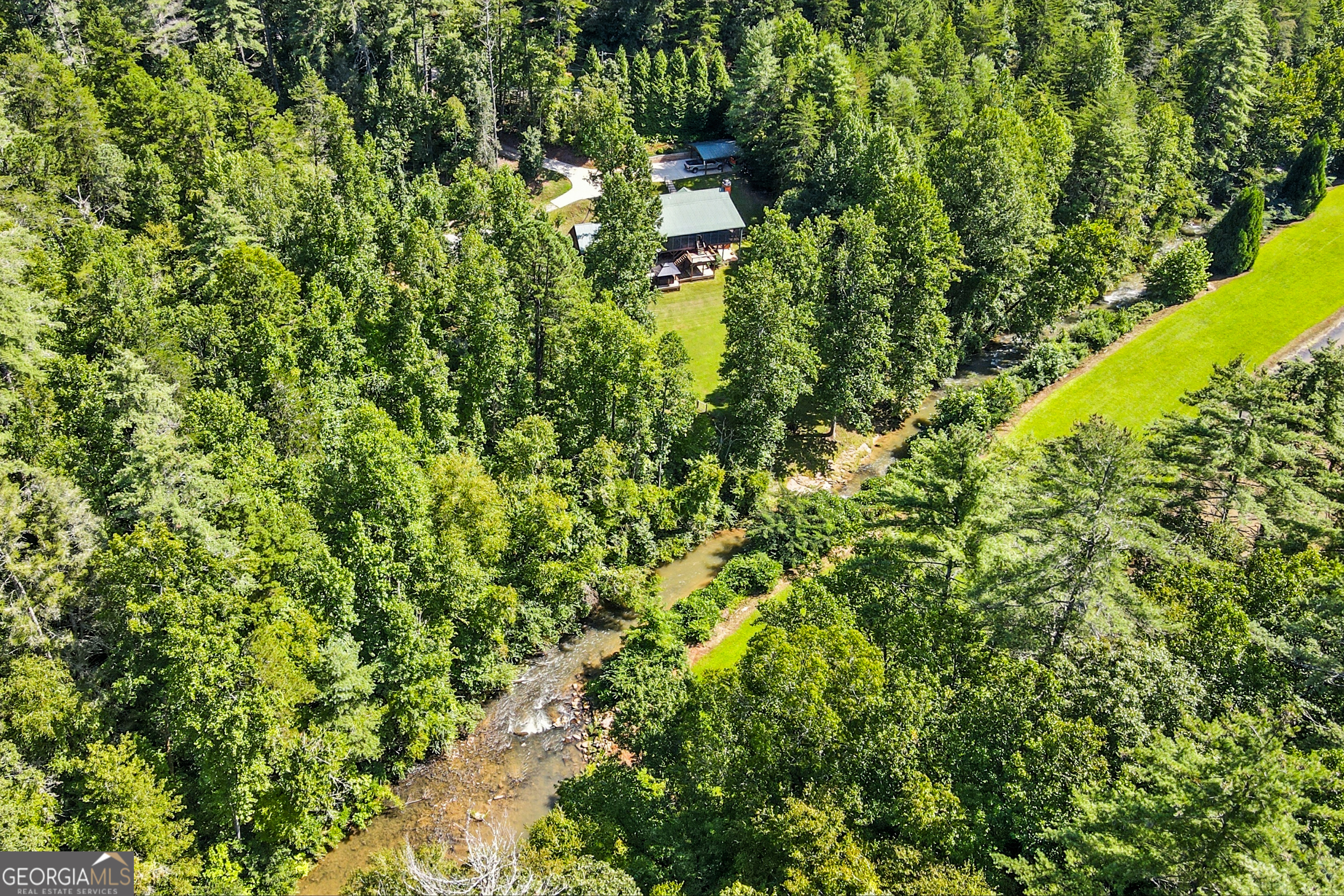 Charming Rustic Cabin Retreat on Stekoa Creek Welcome to this beautiful 4-bedroom, 2.5-bath cabin that perfectly blends rustic character with modern comforts on 2+/- acres. Nestled alongside Stekoa Creek and Smith Branch, this property offers serene water views, a mostly level yard, and a fenced garden space for those who love the outdoors. Step inside to soaring ceilings and a stunning floor-to-ceiling masonry stone fireplace that anchors the light-filled living room. The open layout features wood finishes throughout and pine hardwood floors throughout the main living areas, with cozy carpet and laminate flooring in the lower level bedrooms. A sunroom/screened porch with a swing and dining space, plus a screened porch, invite year-round enjoyment, while the covered lower deck with hot tub provides the perfect spot to relax and unwind. The main-level owner's suite is a true retreat, complete with double vanities, soaking tub, separate tiled shower, and his-and-her closets and access to the upper level porch. Downstairs, you'll find two additional bedrooms, a full bath, and plenty of extra storage. Outside, a 1-car detached garage, 2-car carport, covered storage shed, and beautifully landscaped grounds add both charm and practicality. Whether you're looking for a full-time residence or a mountain getaway, this cabin offers the perfect combination of rustic style, comfort, and convenience.