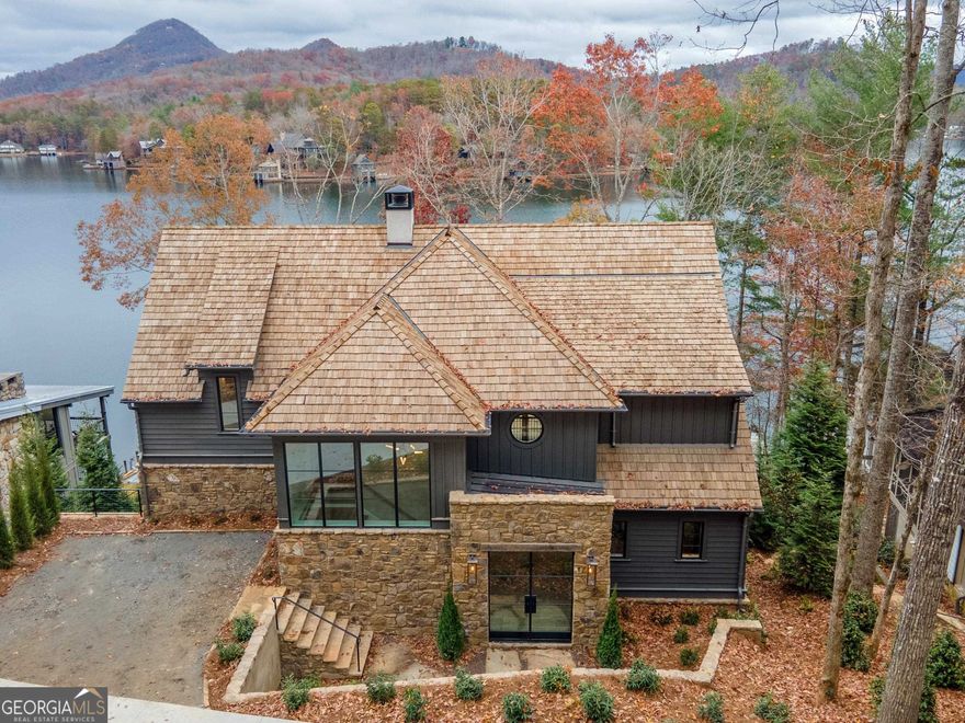 Fee Simple! With 5 bedrooms, 5.5 baths plus a bunk room, this new construction custom home on Lake Burton offers the ultimate luxury lakeside living experience while showcasing incredible long range mountain views. The great room features a vaulted ceiling with antique beams, oak flooring, a plastered fireplace and French doors leading to a lakeside porch with stone fireplace and sweeping lake and mountain views. The designer chef’s kitchen overlooks a lakeside dining area with floor to ceiling custom steel windows framing the lake. The kitchen includes a 48" Wolf Range, 30" Meile refrigerator and freezer columns, ice maker, and custom cabinetry with built-in organization. A walk-in pantry features a 2nd sink and dishwasher, under counter drink fridge and built-in wolf microwave. A powder room and laundry room are located off the foyer. The private main floor owners suite offers lake views, a spa-like bath with oversized shower, double vanity, tub, water closet and walk-in closet with built-in shelving. Upstairs, guests will enjoy 2 private bedroom suites, each with a private bath and lake view, plus an office. The terrace level offers 2 additional guest bedrooms with lake views, a bunk-room with custom built-in bunks, a family room with wet bar/beverage center and access to a covered lakeside grilling deck. The 2-stall boat house on deep water offers incredible northern facing views. Don’t miss this opportunity to skip the building process and move into a brand new home on Lake Burton! *Photos showing Furniture are Virtually Staged