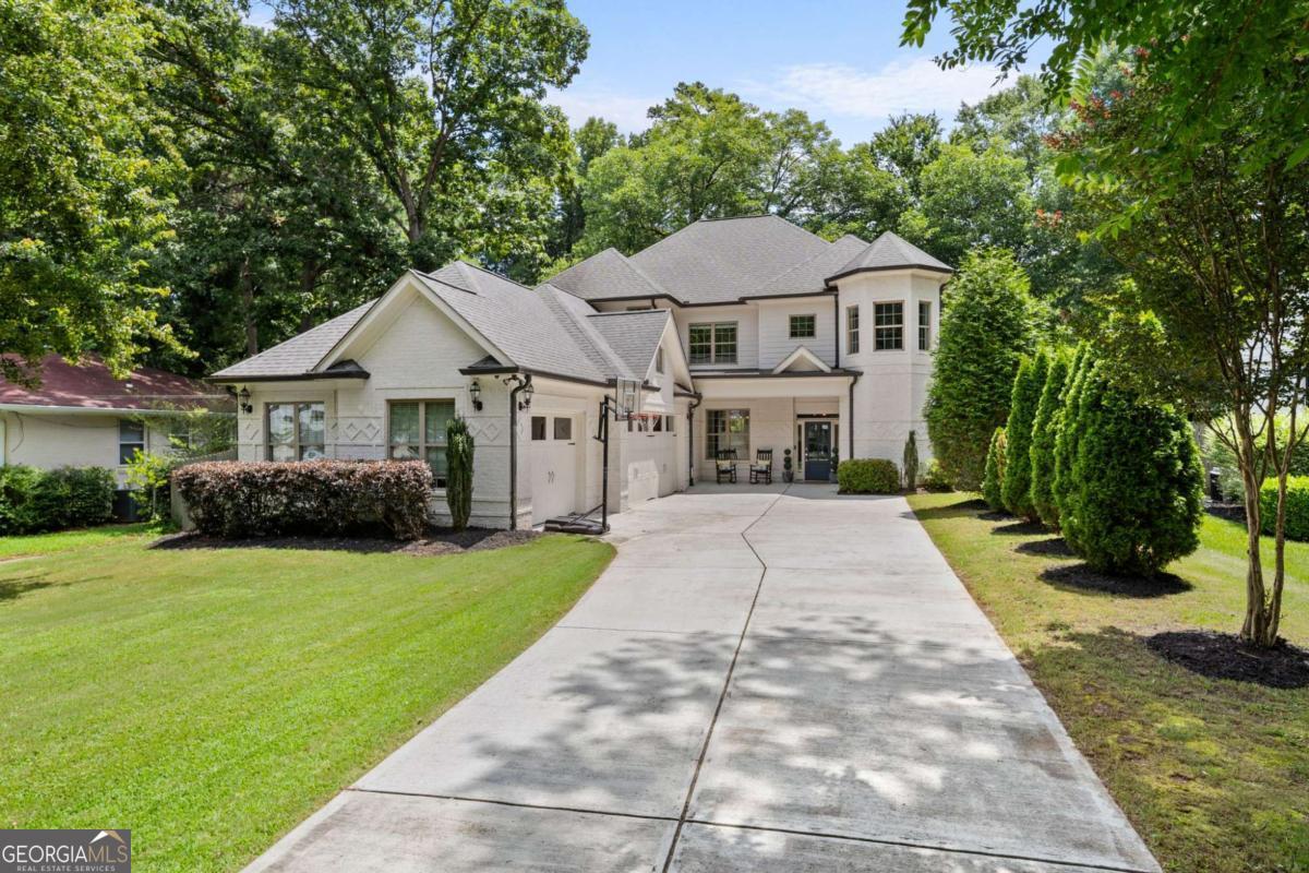 Tucked into one of Brookhaven's most desirable pockets of Ashford Park, this stunning residence sits on a deep, tree lined lot offering privacy and a peaceful residential feel while being just minutes from premier shopping, dining, and parks. A timeless white painted brick exterior wraps three sides of this home, paired with a charming turret-style accent and inviting front porch. The long driveway leads to a 3 car garage and sets the home elegantly back from the street, boosting curb appeal and functionality. Step inside to a bright, spacious foyer that opens to a dramatic dining space beneath an intricate coffered ceiling. Rich hardwood floors and wide-open sight lines lead into an open concept living room filled with natural light, built-in shelving, and seamless access to the backyard. The kitchen impresses with sleek white cabinetry with marble counters, a large island with seating, a high end wolf appliance package, and a walk in pantry designed for both everyday living and entertaining. Just off the kitchen, a tucked away office nook offers a perfect remote work zone. Also on the main level, a private guest suite with a full ensuite bath is ideal for visitors or in-laws, complemented by an additional half bath for convenience. Upstairs, a versatile loft landing serves as a playroom, reading area, or media zone for kids or guests. The spacious primary suite is a true retreat, complete with a private balcony overlooking the fenced backyard and a luxurious ensuite bath featuring dual vanities, a soaking tub, a separate shower, and a generous walk-in closet. Three large secondary bedrooms and a full upstairs laundry room add everyday convenience and comfort. Out back, enjoy a flat, fenced in yard perfect for kids, pets, or future plans to add a pool. Multiple outdoor living spaces including a covered porch make relaxing or entertaining a breeze. Located just moments from Town Brookhaven, vibrant dining along Dresden Drive, upscale shopping in Buckhead, and the convenience of MARTA, this home blends suburban serenity with unbeatable access to the best of city living.