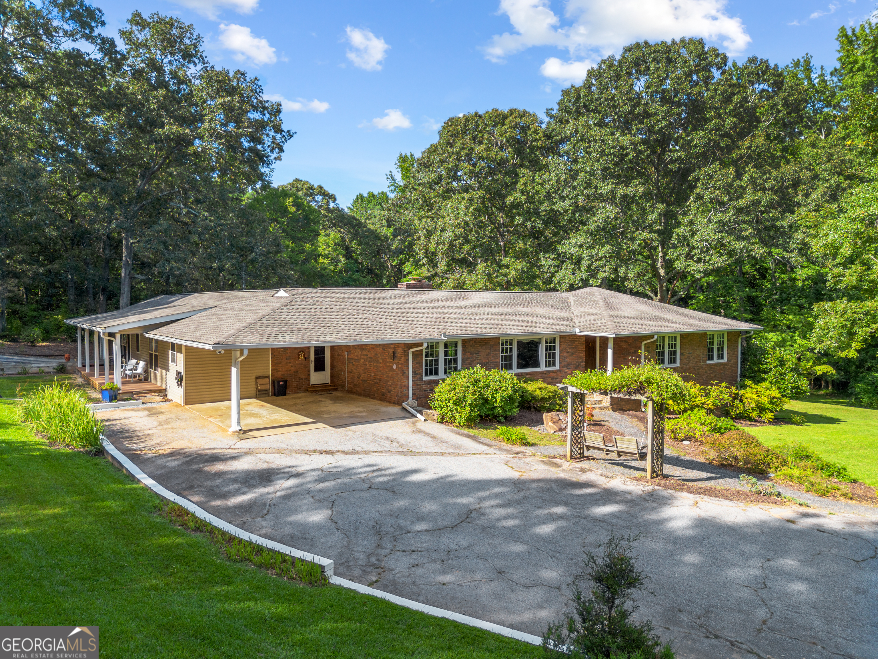 A rare and versatile estate on 5.88 private acres in Snellville. This unique property features a 3-sided brick main home and an attached guest house connected through a shared laundry/mudroom. The main home offers front side brick construction with a brand-new roof (2024), 2 bedrooms and a versatile bonus room, a cozy living room with fireplace, a kitchen with Corian countertops, a main bath with Corian shower and vanity, and a hall bath featuring a cast-iron tub with vintage lavender tile. Additional highlights include a bright sunroom, a spacious covered back porch, a partially finished basement with room for a workshop or storage, a separate A/C unit and water heater, a well-maintained 2-car covered carport, and thoughtful updates throughout. The attached guest house offers its own private entrance via a separate driveway, vinyl siding with a new roof (2024), a spacious living room, a large bedroom with oversized closet, two full baths, and a kitchen with granite countertops. It also features its own A/C unit and water heater, a covered side porch, and a 1-car covered carport, making it fully independent and comfortable for long-term stays or income potential. Outdoor features include a 16x16 powered workshop, RV parking with dedicated septic hookup, a storage barn along with older barns, an old covered well, and mature plantings including five blueberry bushes, a fig tree, and a pear tree. Surrounded by wooded privacy, this property offers peace and space while remaining conveniently located. Most appliances remain, making this estate truly move-in ready for owner-occupants or investors seeking flexibility, space, and endless possibilities. Near shopping.