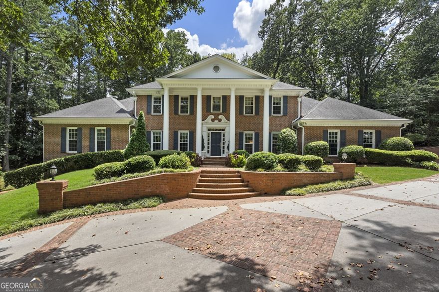 This elegant gated estate rests on 2.23 manicured acres in the heart of Sandy Springs, offering exceptional privacy, architectural sophistication, and an abundance of living space both inside and out. A long, landscaped driveway leads to a grand brick facade with classic columns. The grand double doors welcome you into a breathtaking two-story foyer featuring polished marble floors and a sweeping staircase. To the left, the formal living room invites conversation with its fireplace and abundant natural light, while across the foyer the formal dining room exudes elegance with marble flooring and a mirrored feature wall. The richly paneled den, accented by coffered ceilings and a fireplace, offers a warm and refined space for quiet reading or intimate gatherings. Nearby, a solarium with floor-to-ceiling windows and an antique fountain opens into an expansive media and entertainment room, complete with built-in cabinetry, a retractable awning, surround sound, and dramatic Palladian-style windows that flood the space with light. The heart of the home lies in the gourmet kitchen, with white custom cabinetry, porcelain tile flooring, stainless steel appliances including a built-in steamer, tile backsplash, and off-white Corian countertops. A spacious breakfast room and adjacent sunroom provide stunning views of the backyard, creating a peaceful setting for daily living. The main level also features a large primary suite with dual oversized closets and a private en suite bath, ideal for guests. Upstairs, the luxurious secondary primary suite is a true retreat, highlighted by a lighted double tray ceiling, spa-inspired bath with dual vanities, a jacuzzi tub, and a custom-designed oversized closet. Additional upstairs bedrooms are generously sized and share well-appointed baths, offering comfort and privacy for family and guests. The finished terrace level expands the home's living space with a versatile layout that includes a home office, a full bath, a wet bar, a game area, and direct access to a covered patio. Just off the terrace level, there's ample space to add a custom pool, allowing seamless indoor-outdoor entertaining. On the opposite side of the storage building, there's room for a tennis court or handball court, adding even more recreational possibilities to the estate. Several levels throughout the home and grounds can comfortably host mixed indoor-outdoor gatherings of over 100 people, making it ideal for entertaining on a grand scale. The grounds are equally impressive, featuring brick paver pathways, manicured lawns, classical statues, multiple fountains, and a built-in gas grill-perfect for al fresco entertaining. The guest house features its own three-car garage, providing private accommodations that include a living space with a kitchen, a full bathroom, and a bedroom. This arrangement increases the total garage capacity to five cars. This one-of-a-kind estate offers timeless craftsmanship, thoughtful updates, and premier amenities in one of Sandy Springs' most sought-after neighborhoods.