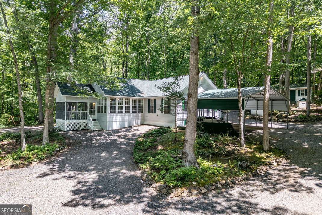 Escape to extraordinary peace, privacy, and natural beauty with this rare 3-bedroom, 3-bath retreat on 2.86 unrestricted acres bordering the protected wilderness of the Chattahoochee National Forest. With a bold, spring-fed creek flowing along its edge, four versatile outbuildings, and immersive forest views from nearly every room, this property offers a lifestyle that blends comfort, creativity, and deep connection to the land. A brand-new roof (installed just one year ago) and a new generator add peace of mind and modern reliability to this already exceptional property. Inside, the home invites nature in with a dramatic glass-walled living room that frames the forest like art, while the sun-soaked rear sunroom and tranquil screened porch offer perfect spots for morning coffee, quiet reading, or evening conversation by the sounds of running water. The open layout allows natural light to spill throughout, creating a warm, welcoming space year-round. Four outbuildings provide endless possibilities-whether you need space for storage, a home office, creative studio, workshop, or guest overflow, these structures add both function and flexibility to the property. The land itself is a woodland sanctuary, where soft gravel trails crunch underfoot, weaving through towering hardwoods that bathe you in cool, dappled light during summer and open in winter to welcome golden afternoon sun. The air is crisp and clean, the scent of earth and leaves ever-present, and the quiet broken only by birdsong, wind in the trees, or the gentle flow of the creek. Multiple fire pits offer places to gather under star-filled skies, while natural landscaping keeps maintenance low and beauty high. Whether you're seeking a full-time home, an artist's hideaway, or a nature-rich family getaway, this is more than a home-it's a soul-filling experience, rooted in the timeless magic of the Northeast Georgia mountains.