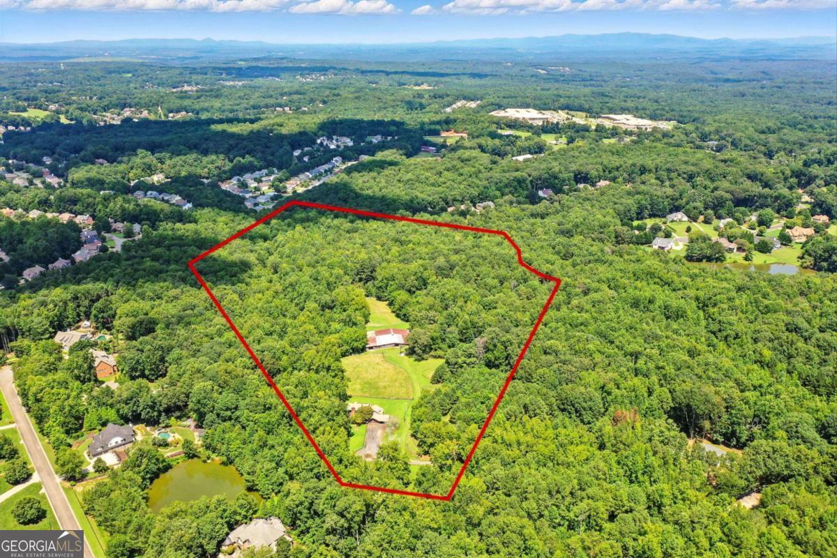 Nestled at the end of a quiet country lane, this idyllic 36-acre property presents a rare opportunity in the highly sought-after Creekview High School district, just minutes from Milton and Alpharetta. Surrounded by estate properties, this private tract blends natural beauty with endless potential. The land features open meadows, mature hardwoods, a flowing creek, and multiple building sites, making it ideal for a private estate, equestrian retreat, or future development. Whether on horseback, ATV, or foot, you'll enjoy scenic trails winding through the woods and along the creek. Equestrian facilities are already in place with fenced and cross-fenced pastures, a 30-stall barn, large arena, and round pen. The barn is thoughtfully designed for efficiency and accessibility, with easy trailer turnaround, designated parking, two offices, a bathroom, multiple tack and feed rooms, hay and shavings storage, and tractor storage: everything needed for a fully operational horse or livestock farm. The residence offers vaulted and beamed ceilings, heart of pine flooring, a cozy fireplace in the primary suite, spacious kitchen, sunroom, and screened porch. With 3 bedrooms, 2 full baths, 2 half baths, a bonus room over the garage, and a workshop, the home provides flexibility-perfect as a barn manager's home, a remodel opportunity, or a suitable place to live while you build your dream estate. This property is truly one-of-a-kind. Whether you envision a private estate, family compound, or development opportunity, you won't find another 36-acre parcel with this much potential in such a prime location. Additional acreage on Pat Rich Road is also available to possibly create a larger development tract. Seller will consider Owner financing