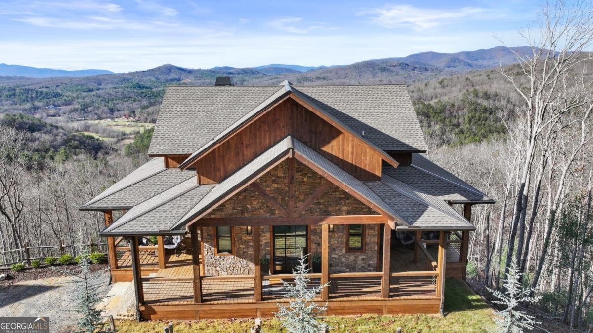 Sunset Ridge - Elevated Mountain Living in Mineral Bluff Set high on Roundtop Road with over four acres, Sunset Ridge offers sweeping views of the Blue Ridge Mountains and more than 4,200 square feet of finely crafted living space. The main level features a dramatic great room with floor-to-ceiling windows, vaulted ceilings, and a statement stone fireplace, flowing into a gourmet kitchen with dual islands, custom cabinetry, and high-end finishes. Four generously sized bedroom suites ensure comfort for family and guests, with two upstairs connected by a unique skywalk and private loft. The terrace level is designed for memorable gatherings-complete with a theater lounge, game area, wet bar, and fireplace-opening to expansive outdoor living spaces. Multiple decks, a fire table, and a hot tub provide opportunities to take in the sunrise, watch the sunset, or stargaze in the cool mountain air. Located just minutes from downtown Blue Ridge, Sunset Ridge blends refined design, exceptional entertaining spaces, and stunning natural surroundings in one unforgettable property.