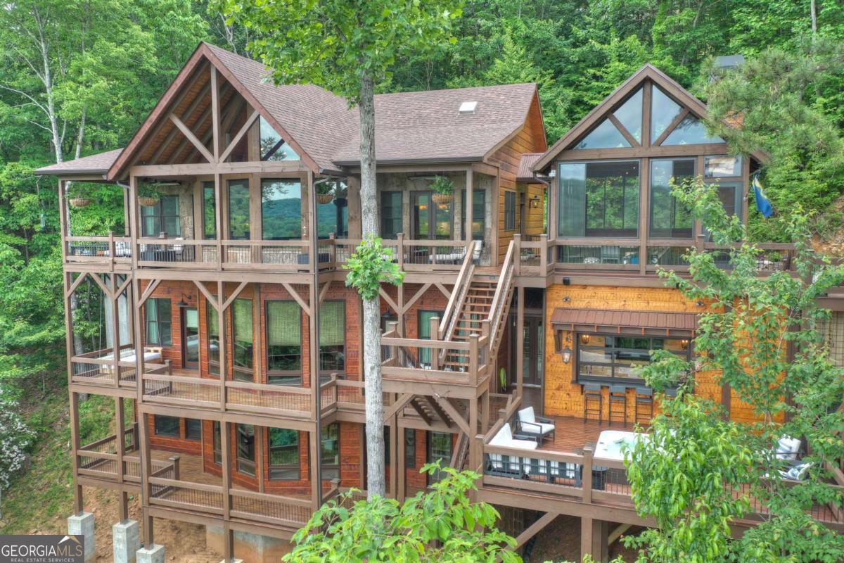 Welcome to Luxury Looks, a refined mountain lodge tucked in the heart of the Aska Adventure Area, just moments from Long Creek Falls, the Toccoa River, Lake Blue Ridge, and endless hiking and rafting opportunities. Framed by layered mountain views, this gated property is designed for both grand entertaining and everyday comfort. The residence offers four bedroom suites and a large bunk room. Two expansive living rooms, each anchored by stacked-stone fireplaces, create warm gathering spaces, while the signature "Bourbon Porch" provides an enclosed outdoor retreat with fireplace, TV, grilling station, and dining space. The terrace level features a full bar lounge with indoor/outdoor flow, a spa-style hot tub area, and a large game room. Porches surround the home with multiple sitting areas and custom swing beds to enjoy the views. A private office overlooks the main living space, while the gourmet kitchen is equipped with high-end appliances, custom cabinetry, and abundant prep space, complemented by formal dining and casual seating. Additional highlights include a large detached workshop shed, full-property backup generators, and a secure gated driveway. Blending rustic sophistication with modern convenience, this estate embodies timeless lodge living in one of Blue Ridge's most sought-after locations. Call today for an exclusive tour!