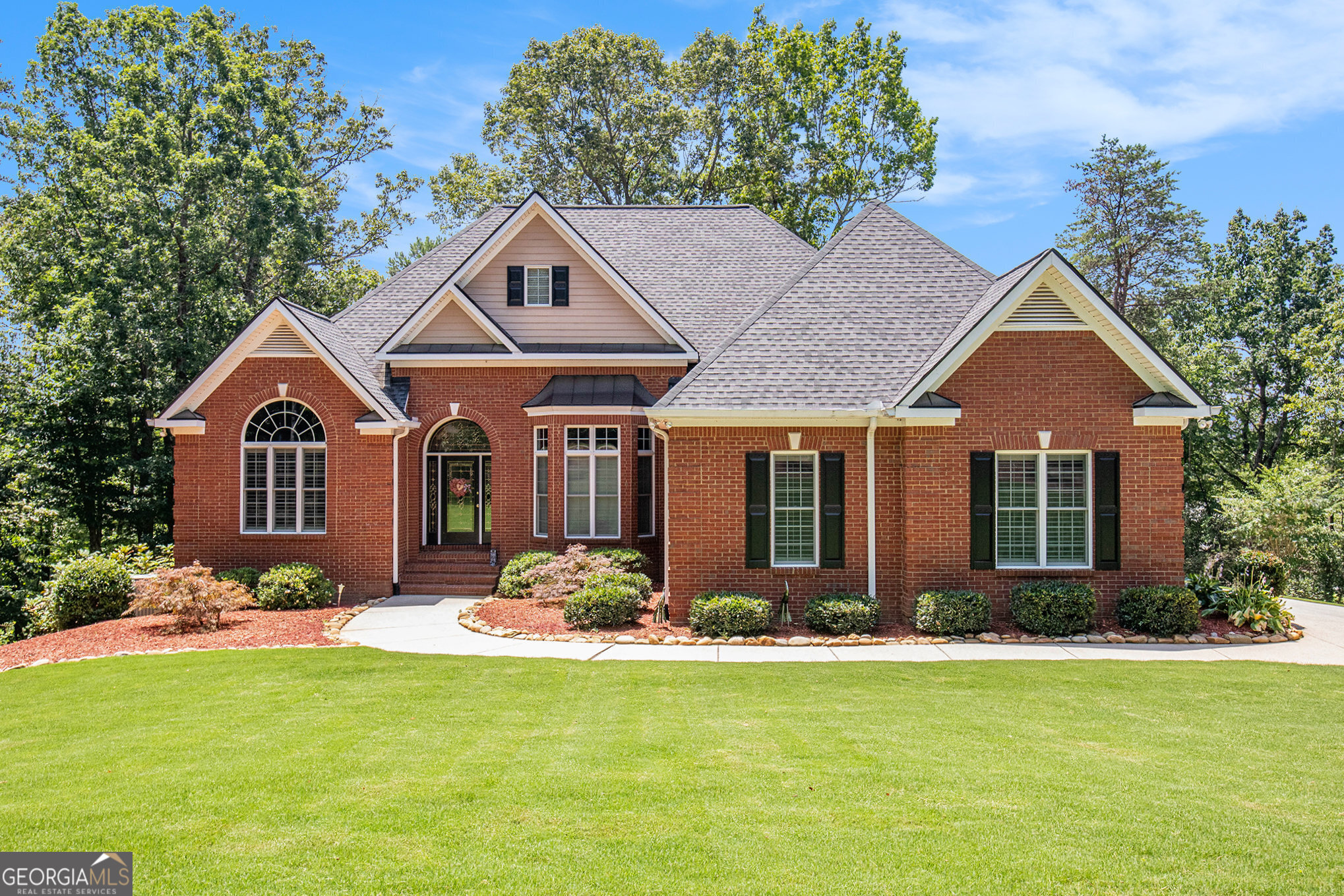 STUNNING BRICK HOME beautifully maintained and nestled on 2.65 acres in the prestigious, gated community of The Orchard Golf & Country Club-located in the scenic Northeast Georgia Mountains. Enjoy breathtaking mountain views and privacy in this exclusive setting. As you enter through the elegant leaded glass front door, you're welcomed by gleaming Brazilian cherry wood floors, soaring cathedral ceilings, and a cozy fireplace in the spacious living room. The formal dining room features crown molding and a dazzling crystal chandelier, adding timeless charm and sophistication. Solid wood plantation shutters adorn every window on the main level, offering both beauty and functionality. The kitchen is a chef's dream with rich alder wood cabinetry, striking granite countertops, a copper sink, and matching backsplash. A sunny breakfast room opens to the rear balcony-perfect for morning coffee with a view. The primary suite includes a luxurious en-suite bath and large walk-in closets, with direct access to the balcony. Two additional bedrooms share a full bath, and there's also a versatile den or library just off the foyer. The terrace level offers a full second living space, complete with a kitchen, bedroom, two full baths, a craft/safe room, and a family room with a gas log fireplace and French doors that open to a brick patio. This level also includes an additional garage with an overhead door-ideal for a golf cart, boat, or workshop. The main-level two-car garage features a brand-new epoxy floor, extra storage, an upgraded electrical panel, and generator hookup. The beautifully landscaped yard includes an underground irrigation system, abundant concrete parking, and charming extras like a treehouse tucked in the woods for endless outdoor fun. The property borders the #2 fairway and includes a peaceful creek along the back. Additional highlights: * Recently painted exterior trim * Roof is only 6 years old * 500-gallon buried propane tank for heating, cooking, and fireplace * Move-in ready and meticulously maintained Select furnishings may be available for purchase. Don't miss your chance to own this exceptional home in one of North Georgia's most desirable communities.