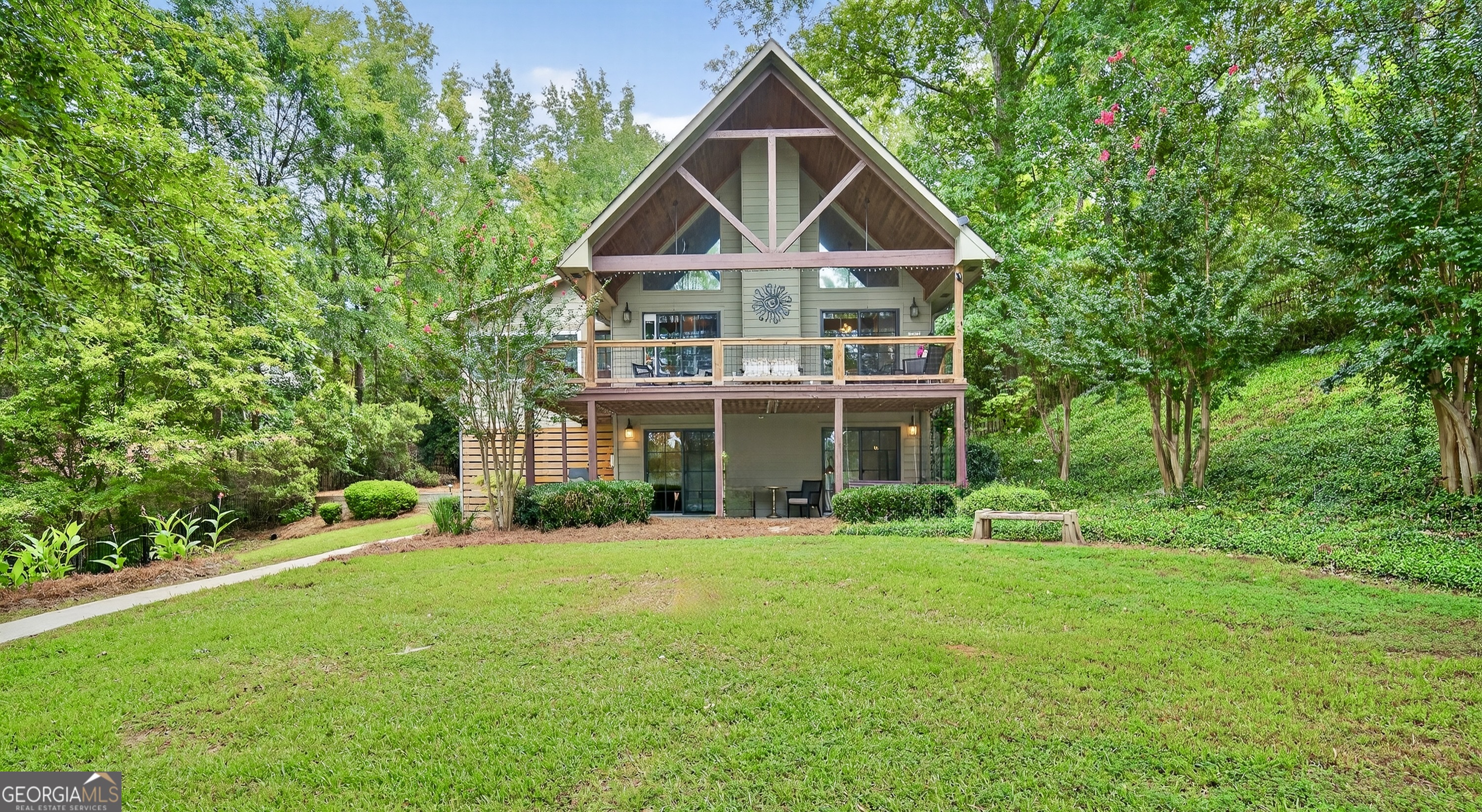 Tucked at the end of a private, shady driveway in the desirable Bluegill community, resides a rare opportunity on Lake Sinclair. With 162 feet of shoreline, a brand-new seawall, and wide open views across a quiet part of the lake, this stunning south-facing home enjoys the benefits of the lake's stunning sunrises and sunsets while the calm water is perfect for swimming, boating, fishing or just relaxing. The outdoor setting is exceptional: huge deck overlooking a manicured lawn, basement terrace and shuffleboard court make for fun family lakeside living. The covered boat dock includes a lift for your boat and wave runner, while the driveway has two powered outbuildings for storing gear or creating a hobby space. Inside, the home blends classic charm with modern comfort. The main floor features soaring A-frame windows that frame the lake and open onto the covered deck. The newly enclosed, climate-controlled sunroom functions beautifully as a dining or sitting room. An oversized primary suite resides on the main level, while the loft bedroom with its own full bath is perfect for company or can be used as an office. The finished basement level offers a second living space with a full kitchen, two bedrooms, and a full bath all opening onto the private lawn. Perfect for guests, extended family, or entertaining. With 2,483 sq ft, 4 bedrooms, and 3.5 bathrooms on nearly 3/4 of an acre, this home delivers space, privacy, and style in one of Lake Sinclair's most peaceful settings.