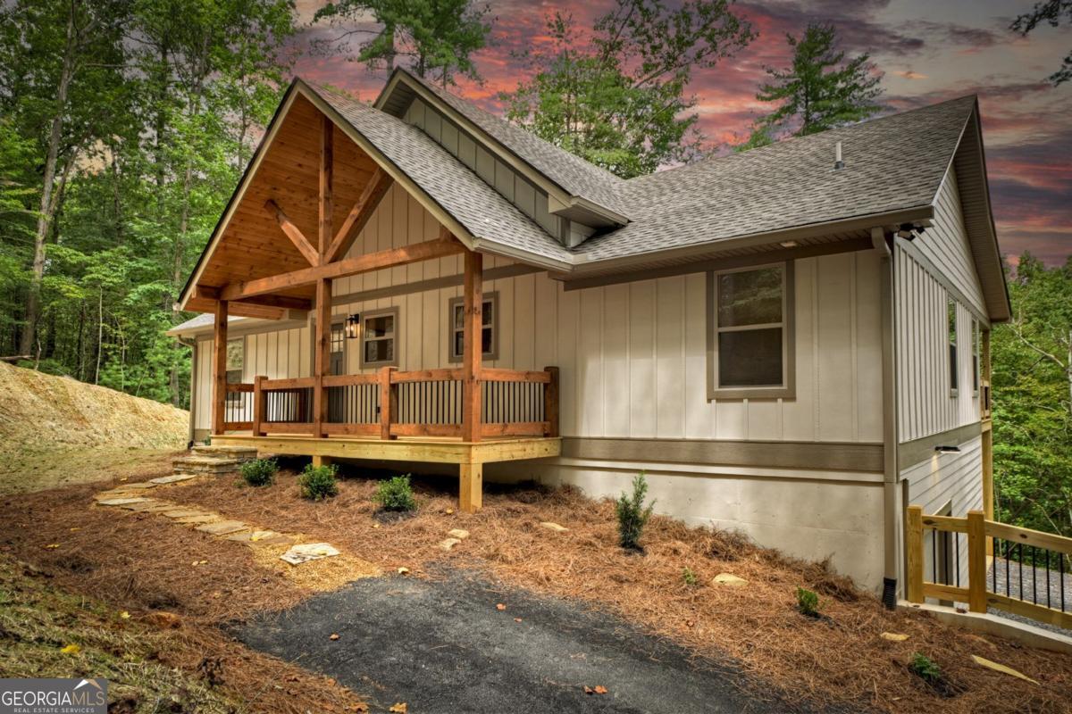 Discover this stunning BRAND-NEW 2025 construction home that blends rustic charm with traditional elegance, featuring rich wood accents and stone details throughout. Enter through the inviting covered front porch into an open floor plan with a soaring tongue-and-groove cathedral ceiling and a wall of windows framing serene treetop views. The custom kitchen boasts a rustic island, quartz countertops, stainless steel appliances, a gas stove, and a walk-in pantry with a barn door. The living area features a floor-to-ceiling gas log fireplace with a Ponderosa wood accent wall. On either side of the home, you'll find a spacious bedroom and full bath. The primary suite includes a vaulted ceiling, private access to the full-length covered deck, and a luxurious bath with double vanities, custom cabinetry, and an oversized tile shower. The second bedroom features a vaulted ceiling, barn door, and full bath with a tile tub/shower combo. The expansive deck, finished with tongue-and-groove vaulted ceilings, offers perfect outdoor living. The full daylight basement is stubbed for a bathroom and offers space for two additional bedrooms, a large family room, mechanical room, an oversized one-car garage and access to a concrete patio through double glass doors. Located in a private setting with wooded views, the home also includes a paved driveway to both the garage and front door with ample parking. Nestled within a gated community offering amenities such as an olympic-sized indoor pool, two outdoor pools, fitness center, game room, river access, dog park, fishing pond, and more-just minutes from downtown Ellijay, hiking, vineyards, and apple houses. Seize the opportunity to own this exceptional, high-quality new construction home!