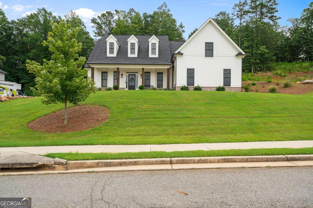 This exceptional property presents a harmonious blend of classic elegance and modern comfort, situated in a highly desirable community. The home's exterior features a welcoming board and batten design with clean lines and striking black window accents. As you step inside, the open-concept floor plan immediately draws you in, with a stunning two-story living area that feels both grand and inviting. Large windows flood the space with natural light, offering views of the surrounding landscape and creating a bright, airy atmosphere. A modern fireplace serves as a central focal point, providing a cozy element for cooler evenings. The main level is thoughtfully designed for convenience and sophisticated living. The gourmet kitchen is a chef's delight, equipped with pristine white cabinetry, quartz countertops, a generous island, and high-end stainless-steel appliances. This space is perfect for preparing meals and hosting gatherings. Adjacent to the kitchen, a separate dining room provides a dedicated area for more formal meals and special occasions, adding to the home's versatile appeal. The owner's en-suite, also located on the main floor, is a private retreat. It features a spacious bedroom with an elevated tray ceiling and an elegant bathroom with a double vanity, a large walk-in shower, and a substantial walk-in closet. Upstairs, the home continues to impress with a flexible layout. A second en-suite bedroom provides an ideal space for guests, offering privacy and comfort. Two additional bedrooms share a well-appointed full bathroom, providing ample space for everyone. The outdoor living spaces are equally impressive. A screened patio with upgraded flooring provides a comfortable, shaded area to relax and enjoy the serene surroundings, regardless of the weather. The .59-acre lot provides plenty of space for outdoor activities and gardening. The community itself offers an array of amenities, including a refreshing pool for beating the summer heat, a volleyball court, and a basketball court, ensuring there is always something to do just steps from your door. This residence is a rare find, offering a perfect combination of style, space, and community amenities. Take the next step toward making this house your own by scheduling a private showing today.