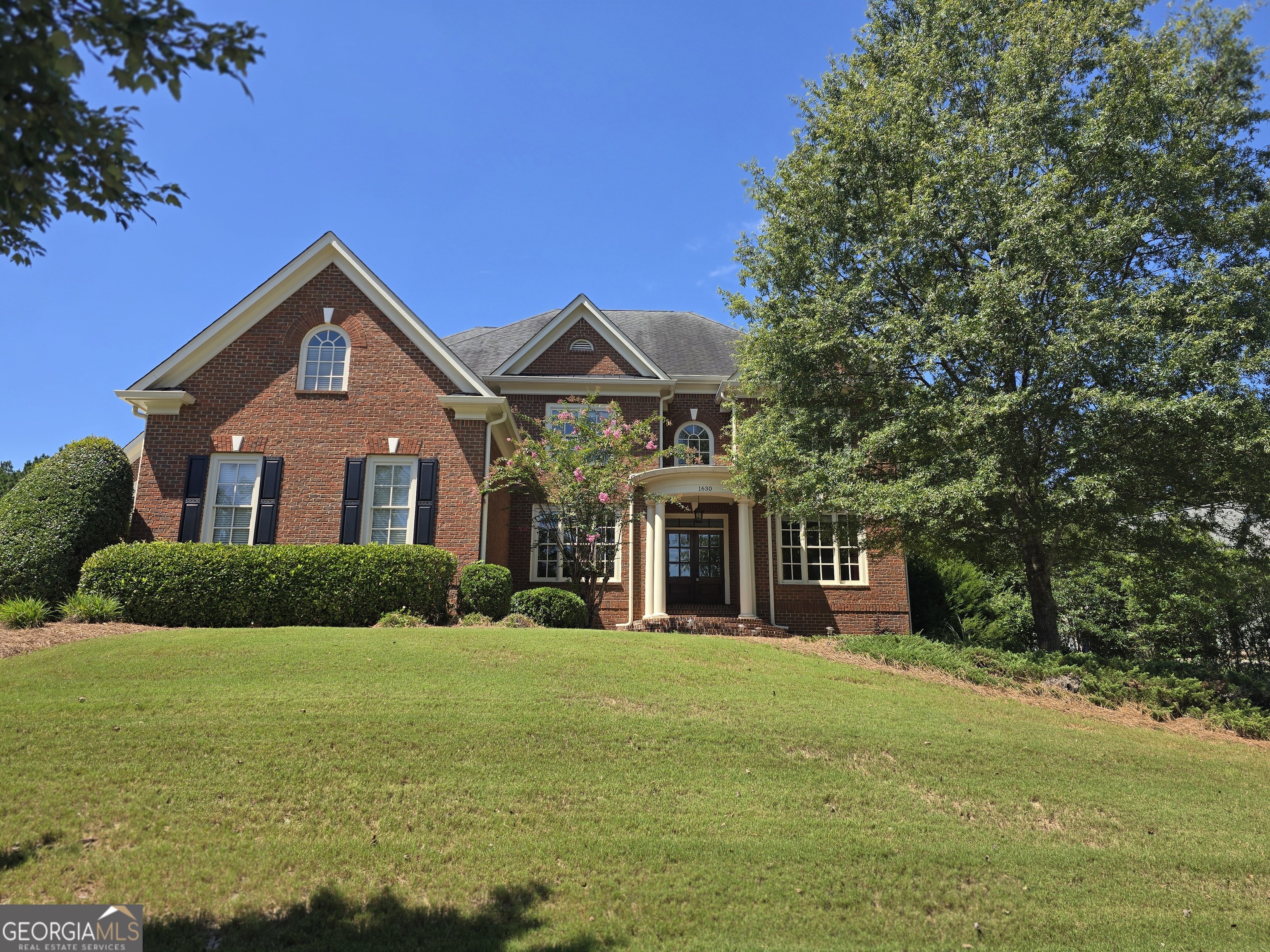 Timeless elegance in The Georgia Club! Welcome to this stately, all-brick Georgian Colonial Revival style masterpiece, where timeless architecture meets modern luxury. From its impressive entry portico and distinguished double-door entrance, this home makes a grand first impression. Step inside to a soaring two-story foyer, flanked by an elegant home office with French doors and a formal dining room. The dining room's butler's pantry-adorned with glass-front cabinetry-creates a dramatic transition into the heart of the home. The two-story family room features a fireplace framed by exquisite traditional built-ins, with arched open shelving above and closed cabinetry below. This inviting space flows seamlessly into the chef's kitchen, where a raised bar island is perfect for entertaining. Guests can enjoy hors d'oeuvres from the elevated bar while you prepare meals on the lower counter. The kitchen is appointed with custom cabinetry, granite countertops, a tile backsplash, stainless steel appliances, double wall ovens, and a built-in microwave. A convenient desk area offers space for homework or home management, while the drop zone near the paneled three-car garage entrance keeps everyday essentials neatly organized. Behind the kitchen, a secondary mudroom opens to the outdoors and provides access-via a split staircase-to an additional two-car garage and the fenced backyard, for an impressive total of five garage spaces. At the rear of the home, a magnificent light-filled room with floor-to-ceiling windows offers endless possibilities-a sunlit living room, formal dining space, or an inspiring home office. The adjacent sunroom showcases serene views of the backyard, blending indoor and outdoor living. A guest suite and full bath complete the main level. Upstairs, the wrought iron baluster staircase leads to a private bedroom with en-suite bath, two additional bedrooms with a Jack-and-Jill bath, and a conveniently located laundry room. The oversized primary suite is a true retreat, with a vaulted ceiling, cozy stone fireplace, and French doors to a spacious sitting area. The spa-inspired primary bath features a tray ceiling, soaking tub on a tiled platform, a walk-in shower with rain head, and an expansive single vanity with two sinks, plus a generous walk-in closet. The full, unfinished terrace level offers limitless potential for customization. Outside, the 0.60-acre lot is an entertainer's dream, boasting a stone outdoor fireplace with seating and a full outdoor kitchen equipped with a gas grill, side burners, and sink-perfectly positioned for your future pool oasis. Located in The Georgia Club, one of Oconee County's most prestigious gated communities, residents enjoy a private golf club with 27 championship holes, tennis and pickleball courts, a fitness center, two restaurants, a community garden, dog park, and more. All this within minutes of shopping, medical facilities, and the University of Georgia (Quarterly lawn maintenance fee of $586). A rare opportunity to own a home that is as impressive in scale as it is in detail.