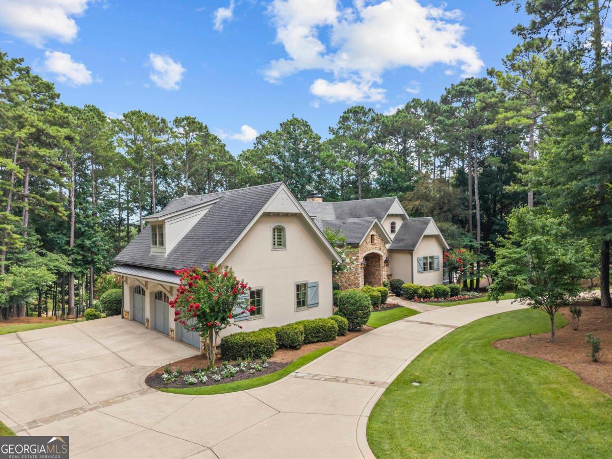 ELEGANT DREAMBUILT ESTATE ON A PREMIER DOUBLE LOT OVERLOOKING THE SIGNATURE 12TH HOLE OF THE OCONEE COURSE WITH A LARGE FENCED BACKYARD AND ROOM FOR A POOL. Nestled on 1.37 acres with a spacious circular driveway and 3 car side entry garage, this custom designed home offers timeless, quality craftsmanship, and breathtaking golf views. This classic French Country estate features 4 bedrooms and a dedicated office with easy potential for conversion to a 5th bedroom, along with 3 and a half baths. The exterior showcases timeless architecture with stone and stucco finishes, a custom solid mahogany front door flanked by gas lanterns, and a soaring two story foyer that opens to an inviting open concept layout designed for the entertainer at heart. The main level great room features beamed ceilings and a floor to ceiling stone fireplace. Triple French doors open to a covered deck overlooking the green of the 12th hole. A built-in wet bar with custom cabinetry, dual lighting, wine fridge, and sink creates a seamless space for hosting. The great room flows into the chef's kitchen, which features a 48 inch Wolf dual fuel range, SubZero side by side refrigerator, Cove dishwasher, custom wood and stucco range hood, and cabinetry with glass transoms and iron accents. A double height granite island anchors the space, while a walkthrough pantry provides built in shelving and extra counterspace. The adjacent prep kitchen includes a second sink, room for a coffee station, and ample space for catering. A custom built in two sided buffet connects the kitchen to the two story dining room, surrounded by windows and filled with natural light, making it an ideal setting for entertaining. The primary suite offers coffered ceilings and French door access to the deck, perfect for quiet mornings and tranquil golf views. The spa like bath features dual water closets, heated floors, soaking tub, walk in shower, a large custom closet, and direct access to the nearby laundry room. Upstairs, a spacious bonus suite includes a sitting area, full bath, room for two queen beds, and a showroom style closet. The terrace level features a second family room, walk out patio, gym, 2 bedrooms with shared bath and separate vanities, and an office with its own exterior access, ideal as a private workspace or potential guest suite. The fenced backyard includes stone walkways, landscape lighting, and room for a future pool. Minutes from the Lake Club, Ritz Carlton, and Creek Club. Membership available.