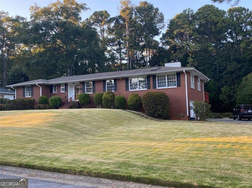 This lovely brick ranch in Cherokee Heights, near Marietta Square, sits on a gorgeous .713-acre lot and features an extra-large deck overlooking a gardener's dream of azaleas and rolling manicured lawns. The home boasts a very large family room with new hardwood floors and a pretty fireplace, three bedrooms, and three full bathrooms, one of which is handicap accessible with a ramp. The hardwood floors throughout the home ensure an easy flow from the formal living room to the spacious family room. The well-designed kitchen includes a charming breakfast room, and a full-sized laundry room/mudroom leads to the spacious deck overlooking the lovely backyard. Additional features include unfinished storage in the basement with a fireproof safe and a two-car drive-under garage in the basement. This home combines classic charm with modern amenities for a comfortable and stylish living experience.