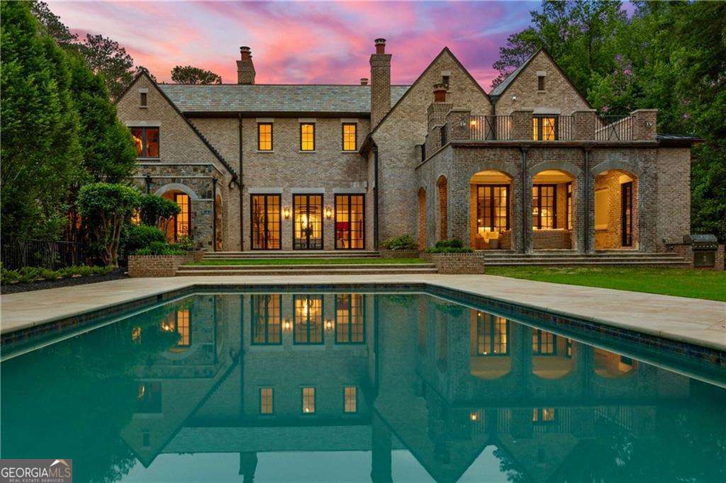 There is extraordinary-and then there is beyond extraordinary. Gracefully concealed behind double gates in Atlanta's premier zip code, Solene at Harris Trail is the epitome of rarefied elegance and architectural mastery. This landmark estate has just been masterfully reenvisioned by the same award-winning firm into one of the most breathtaking homes ever offered in Atlanta. Nestled on 2 gated acres, the property evokes the spirit of a French countryside manor with a tree-lined drive, boxwood hedges, twin fountains, and a motor court concealing five garage bays. The stately facade fuses rustic charm and formal symmetry, featuring limestone pilasters and brickwork with steep gables, a limestone arched entry, and a slate and standing seam metal roofline that crowns the composition with gravitas. A dramatic new steel and glass door opens to the grand foyer, where herringbone white oak floors, silk wall coverings, and bespoke lighting set a tone of refined elegance. At its heart, the double-height rotunda library rises in sculptural form-encircled by curved built-ins, illuminated by a towering bow window, and anchored by a carved limestone fireplace beneath a domed ceiling. A space designed not just to impress, but to inspire. The formal living room continues the elevated aesthetic with coffered ceilings, wide-plank oak flooring, steel French doors, and a fluted limestone fireplace-elevated by a sculptural dual-ring chandelier. Anchored by reclaimed beams, the kitchen and family room blend handcrafted detail with modern sophistication. A Taj Mahal quartzite waterfall island contrasts beautifully with taupe cabinetry, brass dome pendants, and a statement plaster hood above premium appliances. The adjoining breakfast room, wrapped in windows and brick, conjures the ambiance of a European conservatory. Just behind the kitchen, a butler's pantry and bar feature antiqued mirrored cabinetry, marble countertops, and glass-front storage-connecting to the formal dining room, where full-height paneling, a limestone fireplace, and arched window create understated grandeur. A nearby stair offers discreet access to the upper level. Privately situated in its own wing, the Owner's Suite is a private sanctuary. The groin-vaulted ceiling, limestone fireplace, and steel-framed doors open to a secluded lanai with views over the pool and gardens. Dual spa-inspired baths feature marble floors, a sculptural soaking tub, and oversized walk-in showers beneath vaulted ceilings. Boutique closets, a morning bar, private laundry, and a hidden door to the library add layers of thoughtful luxury. The fenced backyard is a resort-style oasis. A gracious lanai off the family room features a cabana bath, outdoor fireplace, and shaded lounge area, next to an outdoor kitchen and event lawn. At the center is a resort-style pool, jacuzzi, and limestone waterfall. Additional features include a putting green, firepit lounge, and a full-sized, lit sports court lined for tennis, pickleball, or basketball. Ascend the grand staircase or private elevator to the upper level, where a hall links six bedroom suites and five marble-clad baths. A second primary suite, upstairs family room with fireplace, additional laundry, and mezzanine library access complete this retreat with future-ready attic space. The terrace level is a world of its own, framed by soaring ceilings and windows that fill the space with daylight. The wellness retreat features an infinity-edge soaking tub, steam shower, sauna, massage room, mirrored gym, and laundry closet. The entertainment wing offers a glazed-tile bar, fireplace lounge, private theater, wine cellar, and a bonus room for hobbies or studio. A private walk-out lawn houses the whole-home generator and completes the estate's seamless indoor-outdoor lifestyle. Solene at Harris Trail is more than a home-it is a masterwork of design, a story of reinvention, and a legacy estate for those who live beyond the extraordinary.
