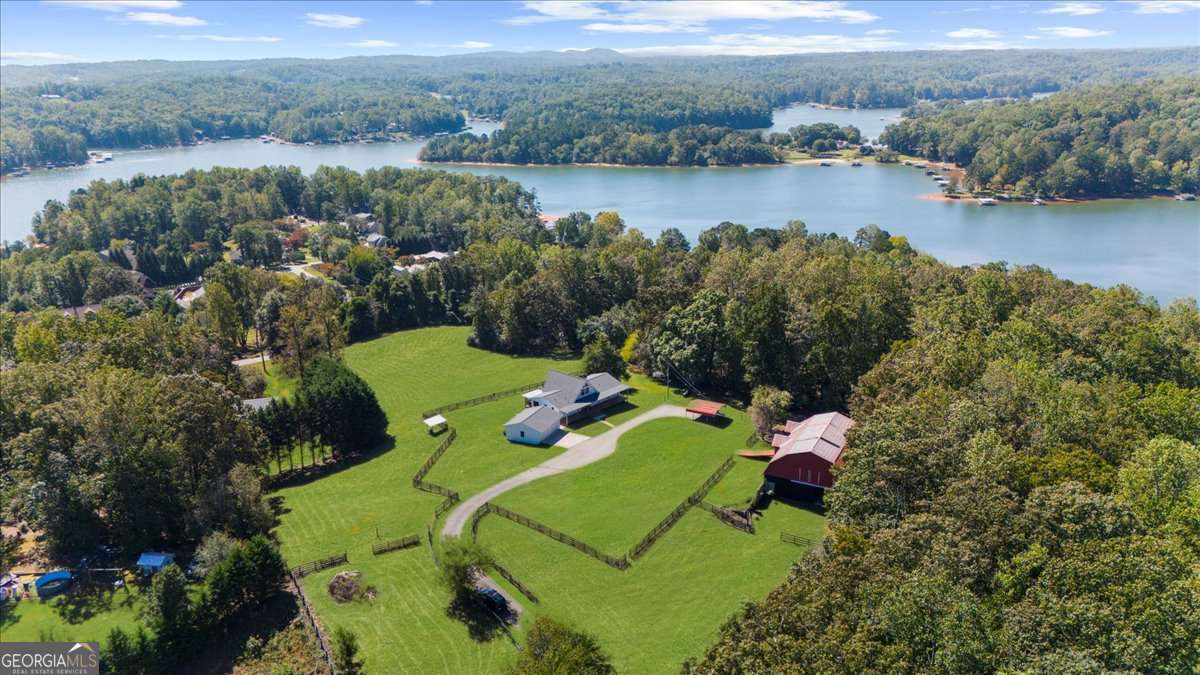 Why settle for land or the lake when you can have both at 518 Overlook Drive? The long, beautiful tree lined driveway leads you to your private gated estate on 7.93 acres with seasonal views of Lake Lanier. This is where you will escape the hustle and bustle life can be and relax at your very own sanctuary of rolling pastures in solitude with your family, friends and farm animals. As you drive in and feel the stress melt away, you are going to love walking up to the charming front porch overlooking the barn and pastures perfect for rocking chairs and a hot cup of coffee in hand. Step inside and be wowed by the soaring vaulted ceilings with natural light pouring through in the great room. Lovely 3" oak floors throughout the main level and loft. The primary bedroom is conveniently located on the main level with picturesque views, brand new, stacking sliding doors (that open all the way) leading to the expansive back deck, and an updated spa-like bathroom. The loft has views overlooking the pastures and lake making it a dreamy office space or an additional sleeping area. The bright and updated kitchen with stainless steel appliances flows into the screened porch where you can cozy up with a nice book and your favorite beverage. The main level also features an updated full bathroom along with a half bath. Make your way downstairs where there is a second kitchen, living room, bathroom and two additional rooms that can be used as bedrooms, home gym, theater, office, etc. This opportunity is rare for MANY reasons and one of those is because of its location being less than 5 minutes to GA-400 providing easy access to the North Georgia Outlets, restaurants and shopping galore in Dawsonville, 25 minutes to the Cumming City Center, and 20 minutes to the charming town of Dahlonega with wineries and hiking trails galore! Another feature that makes this property unique is that it is permitted for a swim platform dock perfect for launching your kayaks from your own backyard, or you can drive 1.5 miles around the corner to Nix Bridge Park and launch your boat from the boat ramp. You'll find a new platform dock in the barn, just waiting to be installed. No HOA means the world is your oyster! There are two road frontages which allows for future expansion whether that's adding additional homesites, a pool, cabana, or a horse arena. The massive barn includes an updated one bedroom apartment with fresh paint and carpet perfect for multi-generational living or potential rental income with a full kitchen, living room, bathroom, laundry room and a covered carport. If you need storage, the barn has no shortage of it on the upper level. The lower level of the barn features four stalls, concrete floors, a tack room with shower, an office and space for all the toys the outdoor enthusiast can dream of owning. Live the life you have been dreaming of right here at 518 Overlook Drive today!