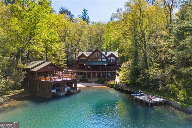 Inspired by the Adirondack Great Camps of the late 1800's and the Great Log Lodges of the American West, this enchanting three-story log house is like nothing else on Lake Rabun. The entire property is accessible with an elevator to all three floors and ramps to all exterior locations. There are 8 bedrooms in the main house and a separate guest suite in the carriage house. This stunningly furnished house is being offered FULLY FURNISHED, "turn key" with the watercraft included. There are currently beds to sleep 24 guests! This property is 2.1 acres, Fee Simple and zoned Vacation Cottage which permits rentals. There is parking for 10 cars on the property. The outstanding location and proximity to the main highway makes this property even more desirable. With paved roads from the main highway to the driveway it's approximately a 10 minute drive to the shops at Lakemont, 15 minutes to Clayton or Hall's Boathouse. Situated directly across from the Dike on Lake Rabun, there is no better viewing for the 4th of July fireworks than from Collins Cove! Custom designed by R.D. Davidson and the owners, masterfully constructed by Larry Gibson with only the finest materials, this house is one of a kind FABULOUS! Enter the front door from the stunning porte cachere or conveniently access by the kitchen door for unloading. The majestic Great Room with 24+ft ceilings, a 24ft tall stone fireplace, tree poles and captivating lake views is jaw dropping! This great room's open floor plan expands further with a wide covered porch that runs the length of the house. The deck's walkway connects to the pavilion style, 2 stall Boathouse with large sun deck and screened porch for ping pong or picnics while enjoying the lake breeze. Savor all the water sport activities the lake offers from the swim dock, the private sandy beach or boathouse. Collins Cove boasts one of the largest private coves and beach on Lake Rabun. Adjacent to the Boathouse is the multi sports court for Pickleball, Badminton or Volleyball. A Firepit and outdoor shower round out the outdoor amenities. The house has two wells and water filtration system along with a "whole house" generator to keep it running smoothly. All that activity stimulates the appetite but a Gourmet Kitchen is prepared to handle crowds with style. With custom made cabinetry and honed granite counters, Thermador appliances, a Thermador 4 burner range with griddle, two dishwashers, two sinks & ice machine, no one will be hungry. The Main Level has two bedrooms, the Primary bedroom suite and a large Bunk room with 4 sets of bunk beds & bath. Also a convenient Laundry room and half bath are on the main level. The Upper Level has 3 Bedroom suites, with two of bedroom suites boasting private balconies to enjoy spectacular views of the lake. The Terrace Level has a cozy entertainment room with fireplace and opens on to the spacious stone patio which leads to the firepit and sandy beach. There is a second Laundry room, and a multi-purpose room for either an office/computer or exercise room Of the 3 Bedroom suites, two have beautiful views of the lake. If you have dreamed of owning a unique lake house and want the BEST of Lake Rabun, THIS IS YOUR DREAM COME TRUE and the house is FULLY FURNISHED AND WITH THE WATERCRAFT!