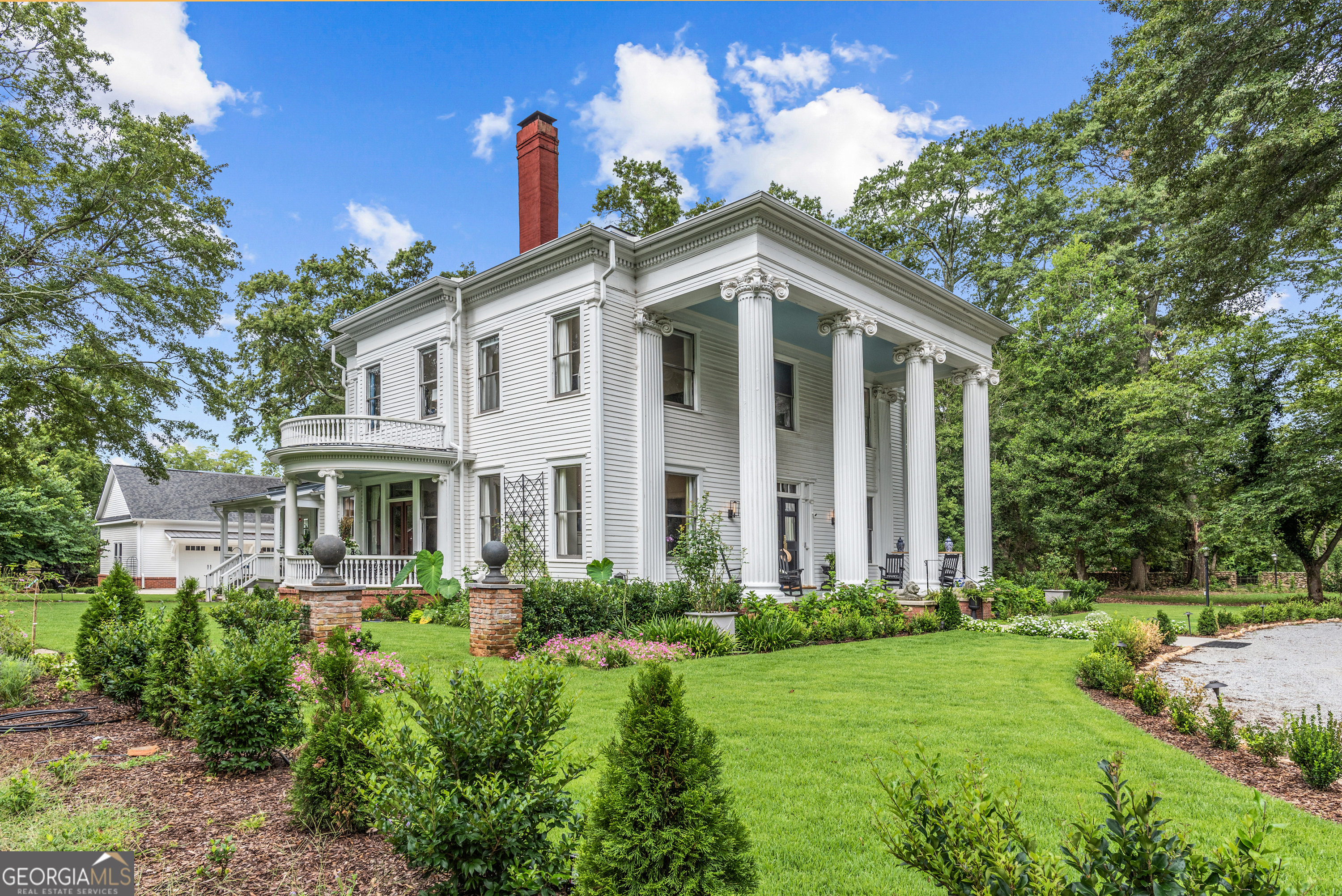 Welcome to Madison Oaks at Poullain Heights-where more than 120 years of Southern elegance and French heritage blend seamlessly with modern comfort and style. Just a short stroll from downtown Madison, you're close enough to hear the courthouse bells toll the passing hours from the town's historic heart. This c.1905 Neoclassical Greek Revival estate, imagined by acclaimed Atlanta architects Denny and Wachendorff, was built by the Poullain family-descendants of Antoine Poullain, who came to America as part of the Marquis de Lafayette's medical team. Lovingly preserved through generations, this home stands as a testament to enduring beauty, history, and thoughtful stewardship. The first impression is unforgettable: towering white columns rise from a landscape shaded by the century-old oak allee and one of Madison's last remaining historic pecan groves. Step into the grand hall, where the original pine floors glow with patina and dual chandeliers light the way to a sweeping staircase. To the right, original glass-paneled pocket doors reveal a moody, modern study. To the left, matching doors open to a sunlit parlor graced with a crystal chandelier and views of the formal gardens. Beyond another set of glass pocket doors, the formal dining room awaits-graciously scaled for grand celebrations, yet warmly intimate for cherished gatherings. It was here, well into the 1950s, that the Poullain family upheld a beloved tradition: Friday night formal dinners where only French was spoken, honoring their heritage with elegance and ceremony. Just off the dining room lies the piazza-a distinctive oval veranda framed by carved balustrades and stately columns. From this vantage point, you're immersed in the tranquility of the Victorian-era garden, centered around a striking 10-foot water feature -a timeless setting for both quiet reflection and festive outdoor entertaining. Toward the heart of the home, the gourmet kitchen is designed for both function and flair: professional-grade stainless appliances, custom local cabinetry, and a new quartzite island. The adjoining breakfast area overlooks both garden and pool-a perfect spot for casual dining. The living room offers a comfortable retreat, recently renovated with coffered ceilings, a cozy fireplace, and a large TV-ideal for unwinding. Two covered porches invite you to enjoy the outdoors all year long. Ascend to the second level and be greeted by the original Art Nouveau stained-glass window-a striking centerpiece once considered a status symbol of early 20th-century home design. It's just the beginning of the refined and elegant experience that awaits upstairs. Wake each morning to the soft glow of sunrise over the formal gardens in a private newly designed Primary Suite. The majestic Ionic capitals of the towering white columns frame your view, while the historic oak allee stretches out in quiet grandeur. This serene, light-filled retreat blends the grace of the past with the comforts of modern luxury-an elevated experience of living in a home rich with history. And there's more: a junior guest suite and an additional bedroom, both thoughtfully appointed, along with an original bathroom that retains its historic charm. Together, they complete the upper level-offering comfort, privacy, and timeless elegance for family and guests alike. Life at Poullain Heights naturally flows to the outdoors. From serene garden paths to the resort- style pool, every corner invites relaxation or celebration. The pool deck is perfect for entertaining and ready for an outdoor kitchen upgrade. Own a piece of Madison's history while enjoying the lifestyle you deserve. Schedule your private tour of Poullain Heights today-your dream home awaits.
