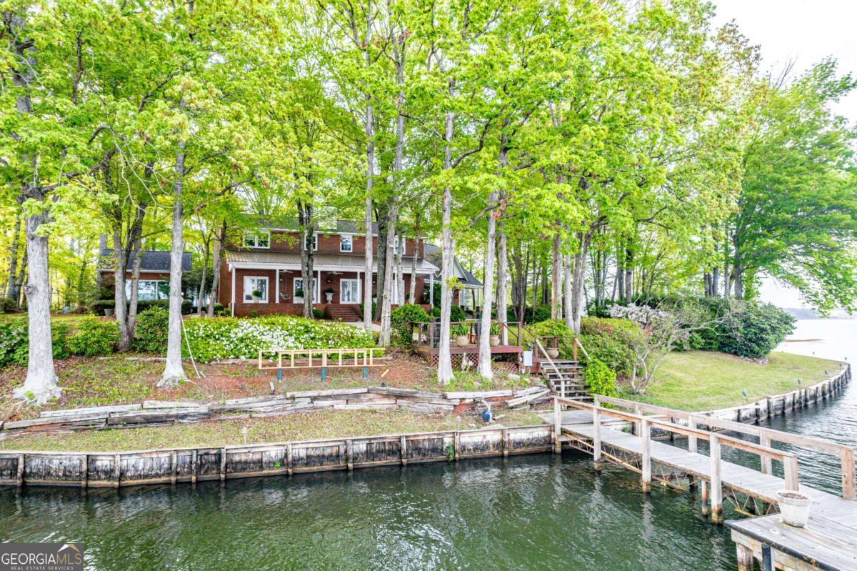 Welcome to 390 David Williams Dr, Sparta, GA where water frontage is in abundant supply on Lake Sinclair. This brick home offers a great deal of privacy and beautiful shaded lake views from its outdoor kitchen and two inviting porches. What sets this property apart is its exceptional four-car garage and a second den/entertainment room above, crafted from solid oak with a cozy, high-end cabin ambiance. Complete with a bar, fireplace, and elevated lake views, this space is ideal for hosting with room for a pool table, card table, and ample seating. Outside, enjoy a spacious outdoor kitchen patio, perfect for outdoor dining against the peaceful backdrop of the lake. Multiple rooms also offer stunning lake views, while a shaded sunroom is great for gatherings and relaxation. Privacy is paramount here, complemented by an outdoor audio system that enhances the ambiance throughout the property. Embrace a piece of Sinclair history with the renowned "Dino home," offering a unique blend of comfort, style, and lakeside charm. Don't miss the opportunity to make this exceptional property yours-schedule a showing today and discover your own slice of lakeside paradise. Georgia Power lease lot fees apply.