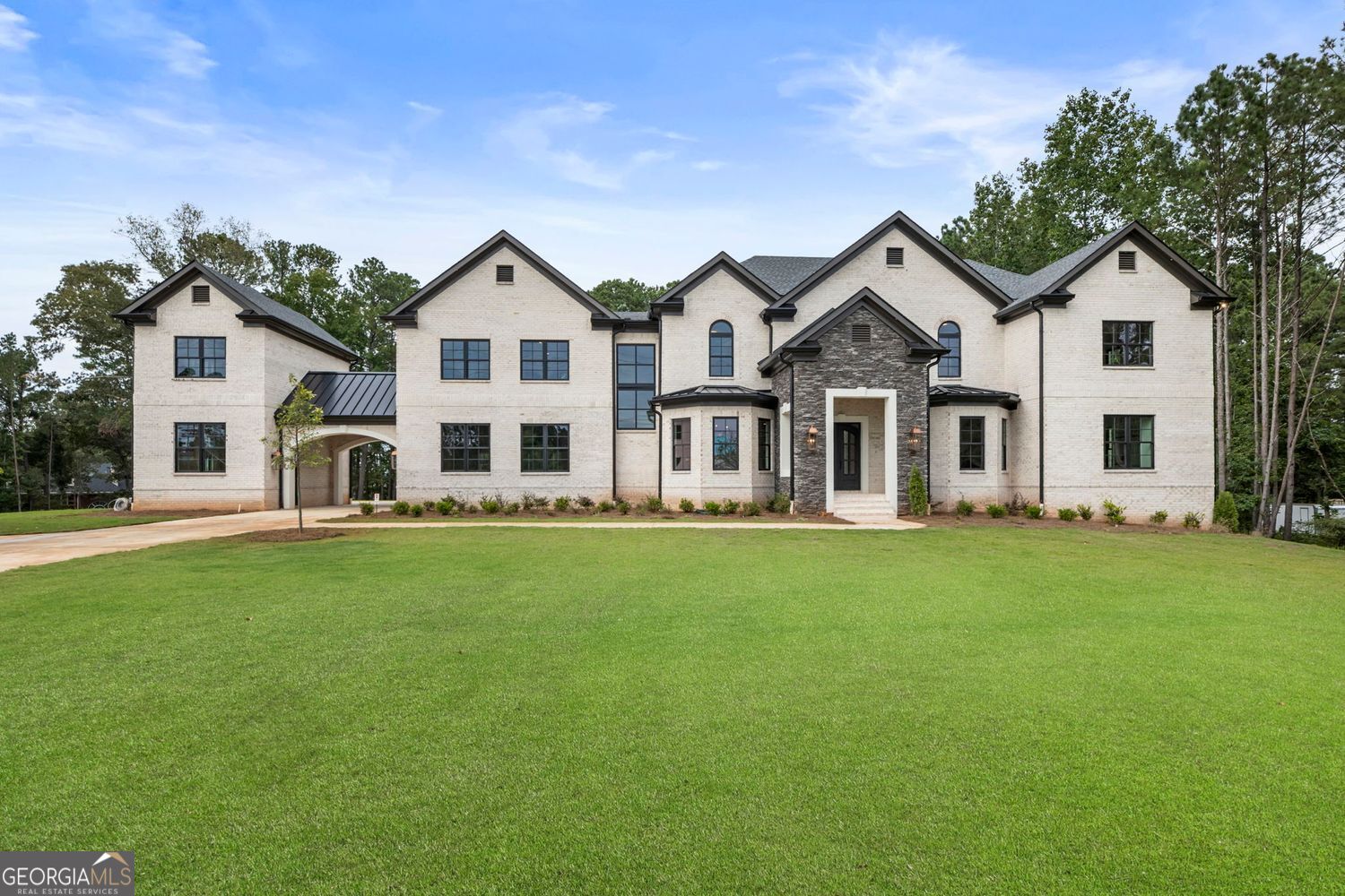 Welcome to Milton's Thompson Manor, a newly built estate on 1.83 acres with the rare advantage of NO HOA. This freedom allows you to enjoy your property on your own terms while still being surrounded by the beauty and prestige of Milton living. Clean lines, expansive windows, and soaring ceilings set the tone for a home that balances modern design with classic function. A covered front porch and iron-and-glass double doors open to a dramatic two-story foyer with custom trim and a curved iron staircase. An office filled with natural light provides a private workspace, while the open-concept main level seamlessly connects the living room, chef's kitchen, butler's pantry, and grand room. The kitchen features custom-stained cabinetry, quartz countertops, a waterfall-edged island, and professional Thermador appliances, including a 48" gas range and 48" built-in refrigerator. A floor-to-ceiling stone fireplace anchors the keeping and grand rooms, while folding glass doors extend the living space to the covered porch with its own fireplace, grilling area, and private wooded views. The main-floor owner's suite is a retreat of its own with a spa-like bath-soaking tub, dual rain showers, and dual vanities with lighted mirrors-plus a custom walk-in closet with integrated laundry. Upstairs, four en-suite bedrooms, a loft retreat, and a secondary laundry center add convenience. A full in-law suite offers its own kitchen, living space, and private entry, creating independent yet connected living. Additional features include a porte-cochere linking three garages with epoxy floors, EV connection, pet wash station, and optional finishable space above. The unfinished terrace level offers endless options for future customization. Located in the heart of Milton, residents enjoy award-winning public and private schools, locally owned restaurants, and proximity to Crabapple, Alpharetta, Avalon, and GA-400-all while enjoying the freedom that comes with a NO HOA lifestyle