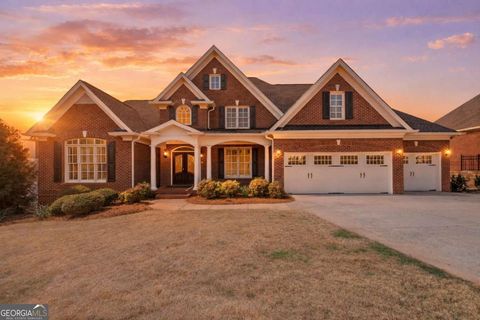 Stunning single-family residence in Flowery Branch, GA, featuring a brick exterior, inviting porch, and a spacious driveway, set against a picturesque sunset backdrop.