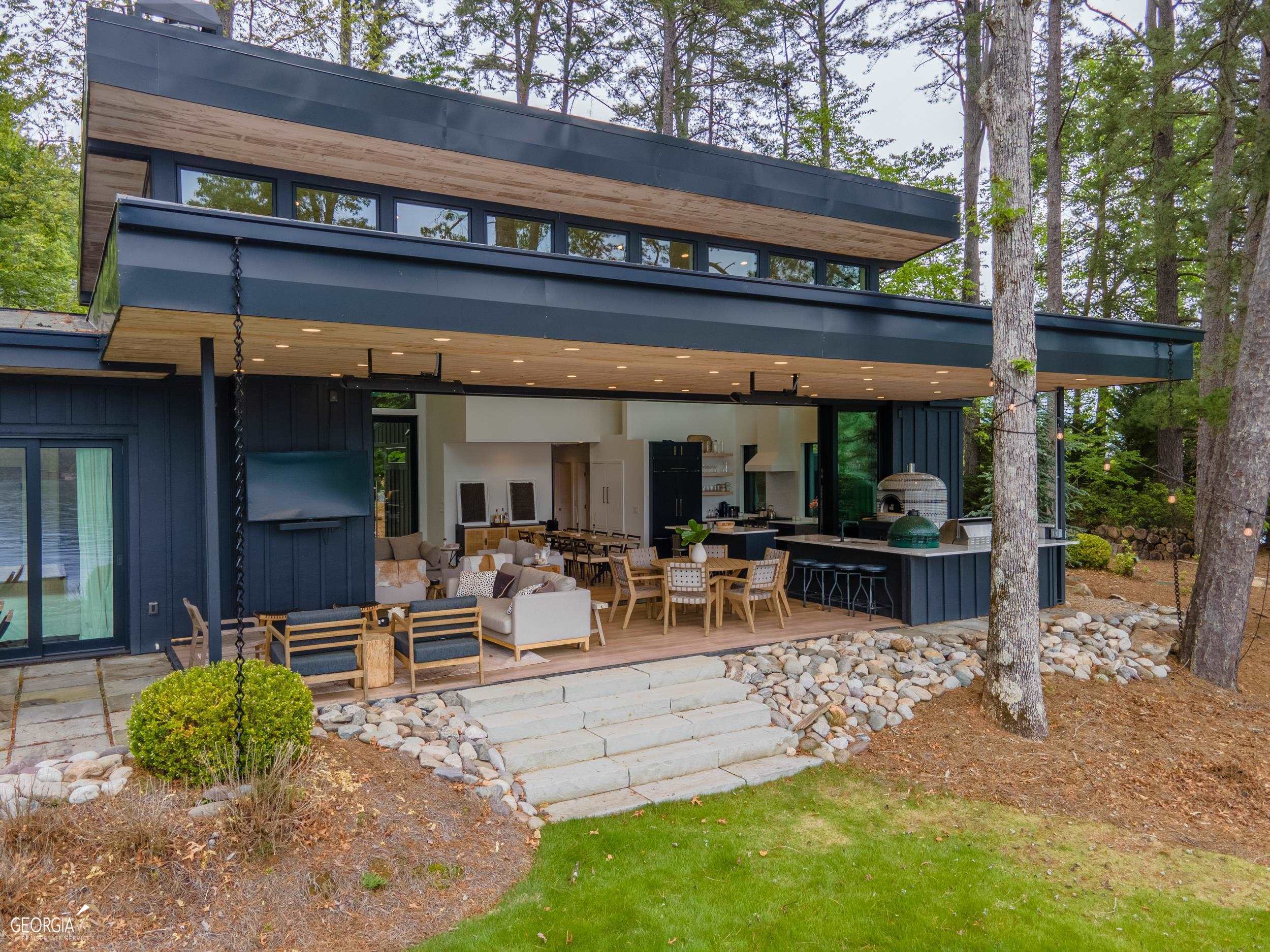 Welcome to this modern lakefront oasis on the stunning shores of Lake Burton. This exceptional modern home boasts 4 bedrooms, 3.5 baths, a bunk room and an inviting open floor plan designed to maximize comfort and enjoyment. As you step inside, prepare to be captivated by the seamless blend of indoor and outdoor living spaces, perfect for entertaining or simply relaxing in the embrace of nature's beauty. The highlight of this exquisite residence is the telescoping door that effortlessly opens to create a harmonious flow between the great room and kitchen, extending the living area to the great outdoors. Revel in the serenity of the surrounding lake and mountain views as you unwind by the gas fireplace in the great room, which also features a dining area accommodating eight or more guests. The well-equipped kitchen is a chef's delight, offering everything you need to create culinary masterpieces. For those who appreciate the art of al fresco dining, the outdoor lakeside kitchen is an absolute delight. Indulge your senses with a wood-burning Forno Bravo pizza oven, a Lynx power burner, a Sedona gas grill, a Green Egg, an under-counter fridge, and a sink, ensuring every outdoor cooking experience is an absolute pleasure. Immerse yourself in the beauty of the outdoors on the covered porch, complete with a gas firepit, where you can savor breathtaking views over the long-range lake and mountain vistas. The two-story boathouse features an oversized top deck where you can marvel at the spectacular 4th of July fireworks illuminating the night sky, creating an unforgettable experience for you and your guests. The level point lot is a rare gem, offering a flat lawn and a beach area for enjoying lakeside recreational activities. With its seamless blend of indoor and outdoor living, breathtaking views, and attention to detail, this home is the epitome of modern elegance and serenity. Don't miss the opportunity to make this extraordinary retreat your own! Additional features include: Radiant heated bathroom floors, pre-wired for EV charger at house and boathouse, full house generator, Hot Springs Hot Tub, built-in ceiling heaters on porch and outdoor shower.