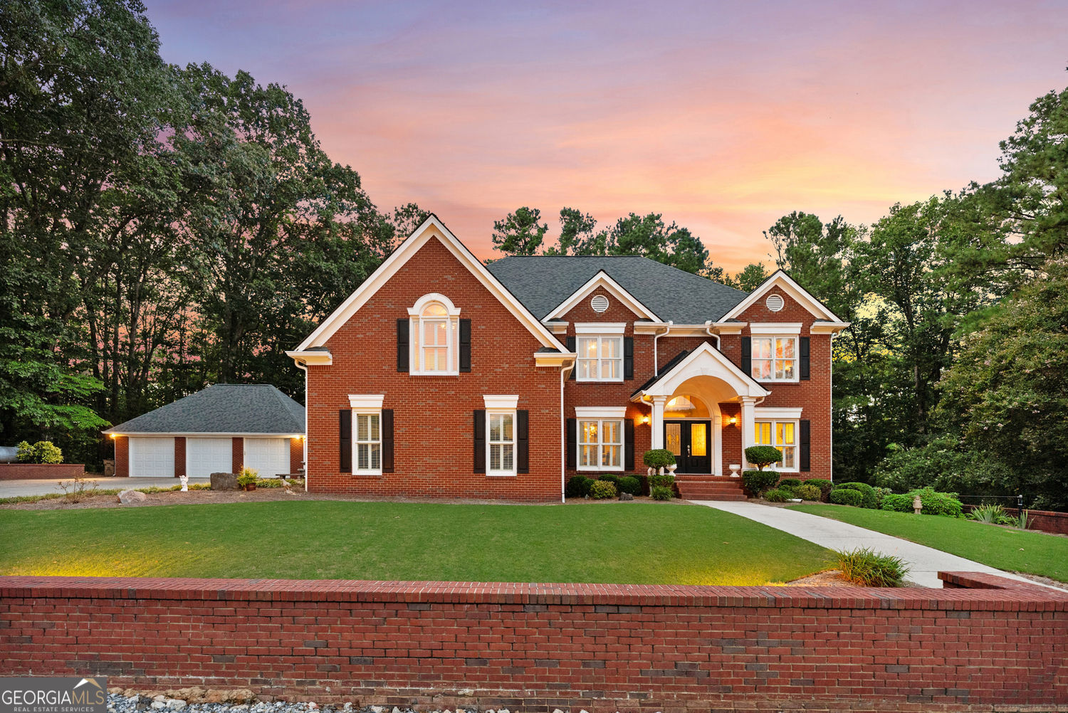 Nestled on 21.8 acres in the heart of Milton and bordering The Manor Golf & Country Club, this versatile equestrian estate blends classic Georgian architecture with exceptional outdoor amenities. The main residence features six bedrooms, five and a half bathrooms, and 5,406 square feet of finished living space. An oversized two-car attached garage and a three-car detached garage, both with insulated doors, provide abundant parking and storage. Interior upgrades include plantation shutters, granite kitchen countertops with slide-out trays in the lower cabinets, and recently replaced Legend windows. The home also boasts a newer roof (2018) and multiple new HVAC systems (2022-2024). The gated entrances (separate but connected for barn and house) lead to rolling pastures, mature hardwoods, and over a mile of scenic trails and walking paths. A picturesque and private pond stocked with bass, a charming, covered bridge, and a meandering spring-fed creek create a serene setting perfect for nature lovers. Equestrian facilities are thoughtfully designed and feature a 7-stall center-aisle barn with 12-by-12 stalls, a tack room, wash rack with hot and cold water, and barn-length garage storage. Above the barn, a one-bedroom, one-bathroom full apartment provides comfortable accommodations. A separate four-bay equipment building with 13-foot roll-up doors is ideal for trailer parking and farm equipment. The 200' x 100' riding arena with M10 base and river sand footing, three large, fenced pastures, and separate barn driveway with ample turnaround make horse care and training a breeze. Additional highlights include two wells, one for the house and one for the barn, an outdoor fireplace, a built-in grill, and a gazebo. The location offers exceptional convenience, just 15 minutes from Avalon, Downtown Alpharetta, Halcyon Forsyth, and GA-400, and is zoned for the highly sought-after Cambridge High School. This rare property combines the serenity of a private retreat, the convenience of an in-town location, the elegance of classic timeless architecture, and the functionality of a fully equipped working equestrian farm.