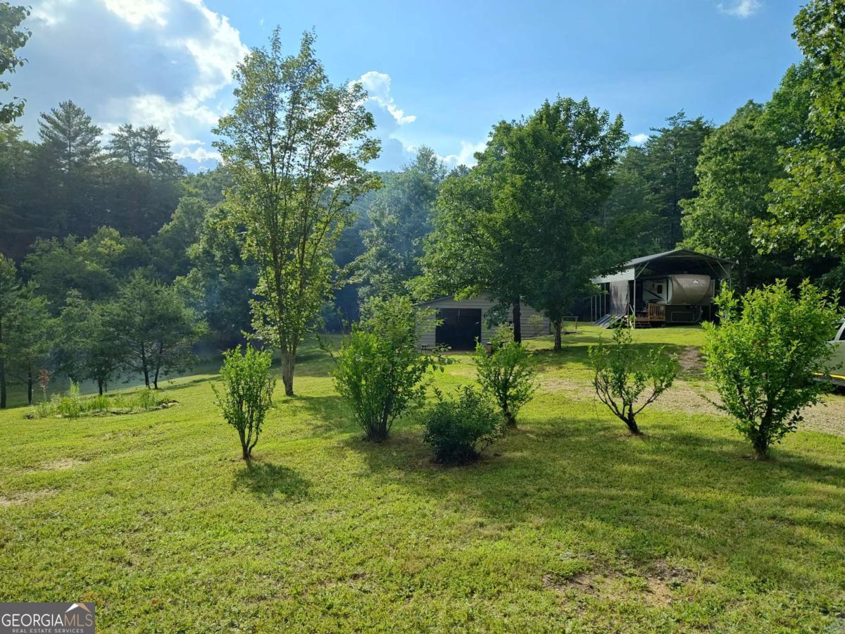 Welcome to your own slice of North Georgia paradise! This 1.794-acre unrestricted property offers a gently rolling, fully usable terrain with mature white oaks, fruit trees, and a beautifully landscaped grassy yard-perfect for gardening, raising small animals, or creating a sustainable lifestyle. With no HOA or association fees, you'll enjoy the freedom to make this property truly your own, whether you're looking to homestead, host, or simply escape to the mountains. The land is well improved, featuring a 30x40 metal shop on a concrete slab (plumbed for a bathroom, kitchen, and laundry) with an insulated ceiling and wood stove-ideal for a workshop, studio, or future living quarters. A second structure, affectionately called "The Pour House" by the current owners, resembles a nostalgic one-room cabin and is perfect for entertaining, with a perfect covered "rocking chair front porch" and rear storage room perfect for tools and the likes! For those who travel or welcome guests, the property includes two separate RV hookups-one for your personal use and a second for friends or family to join you in the mountain experience. A 16x40 RV carport offers excellent coverage, and a well-maintained 2014 Redwood RW38BR14 fifth wheel is included with the sale (via separate bill of sale). With all utilities already in place, this property is truly turn-key and ready for immediate enjoyment-whether you're dreaming of a peaceful retreat, a full-time homestead, or a multi-purpose getaway in the heart of nature.