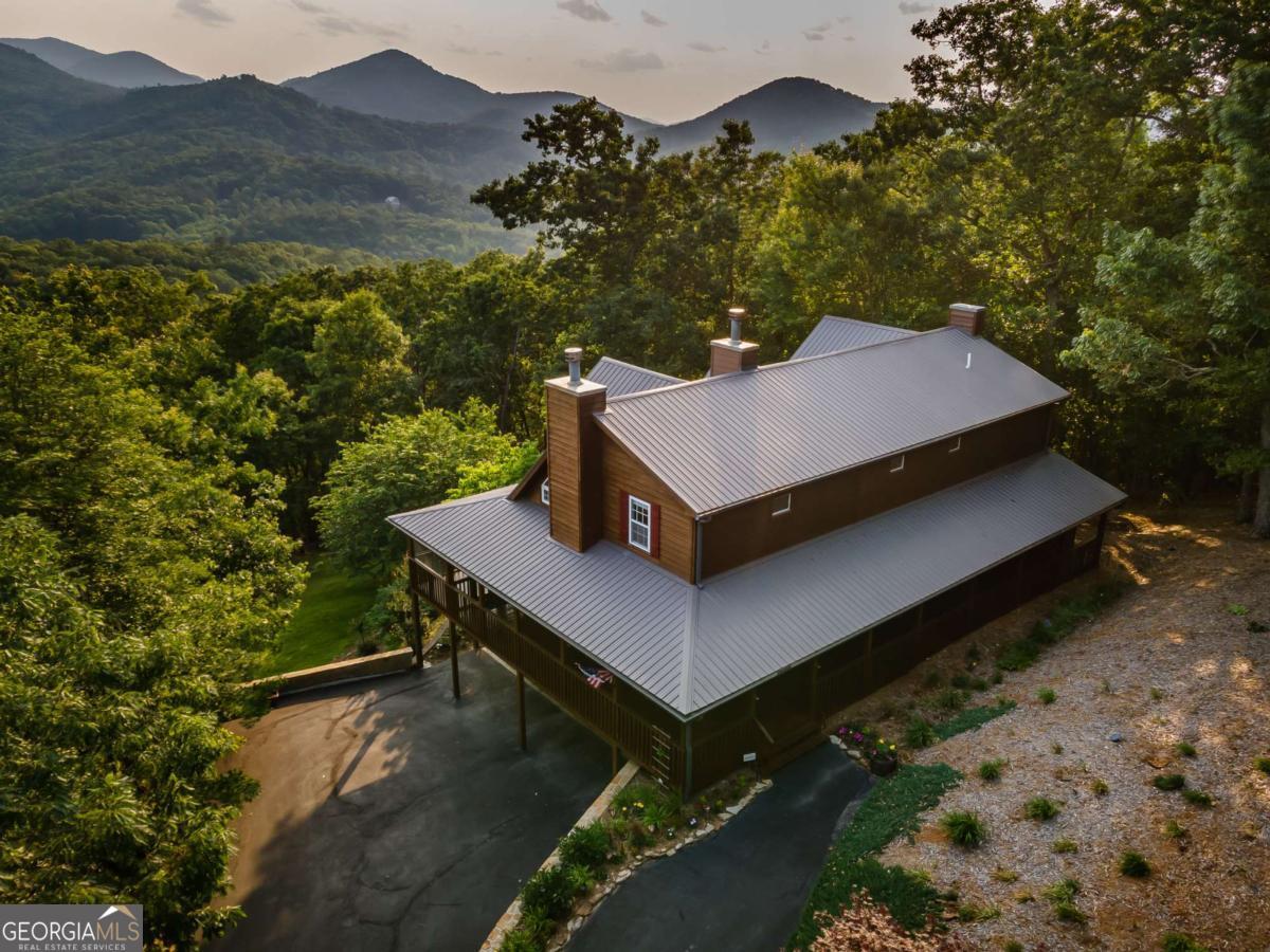 Experience unmatched luxury & serenity on over 3 acres of meticulously landscaped grounds, framed by panoramic, year-round views of the North Georgia mountains. Set against this stunning backdrop, the property is a true retreat that captures the essence of mountain living with elevated style. Built in 2000 & well maintained, the 1.5-story layout is ideal for entertaining & peaceful retreat. The grand great room sets the tone with soaring vaulted ceilings, rich wood flooring, & a dramatic wood-burning fireplace, flowing seamlessly into a light-filled breakfast room & a gourmet kitchen adorned with granite countertops. The main-level owner's suite offers serene mountain views & features plush carpeting, a spa-inspired ensuite with tile flooring, a laundry closet, & direct access to the screened & covered rear deck-an idyllic spot for morning coffee or sunset relaxation. Upstairs, the lofted 2nd level includes 2 beautifully appointed en-suite bedrooms: one with a gas fireplace, designer tile finishes, a soaking tub, & heated floors for added comfort; the other featuring a vaulted ceiling, wood-burning fireplace, statement barn-style wood door, & a private bath. A versatile sunroom with tile flooring offers the ideal space for a home office, playroom, or optional 4th bedroom. The partially finished terrace level includes a full bath with vinyl flooring & ample workshop or storage space, along with an oversized double-bay garage & generous parking. Modern upgrades include upgraded HVAC systems, a durable metal roof, & 2 tandem climate-controlled garages accommodating up to 4 vehicles. Enjoy seamless indoor-outdoor living with low-maintenance wrap-around covered porches, screened front & rear decks, a gentle rolling landscape, & paved access via an asphalt driveway. This exceptional property includes an adjacent 1.9-acre lot, offering space, privacy, & investment potential-perfectly suited for those seeking a private mountain haven & beautiful natural surroundings.
