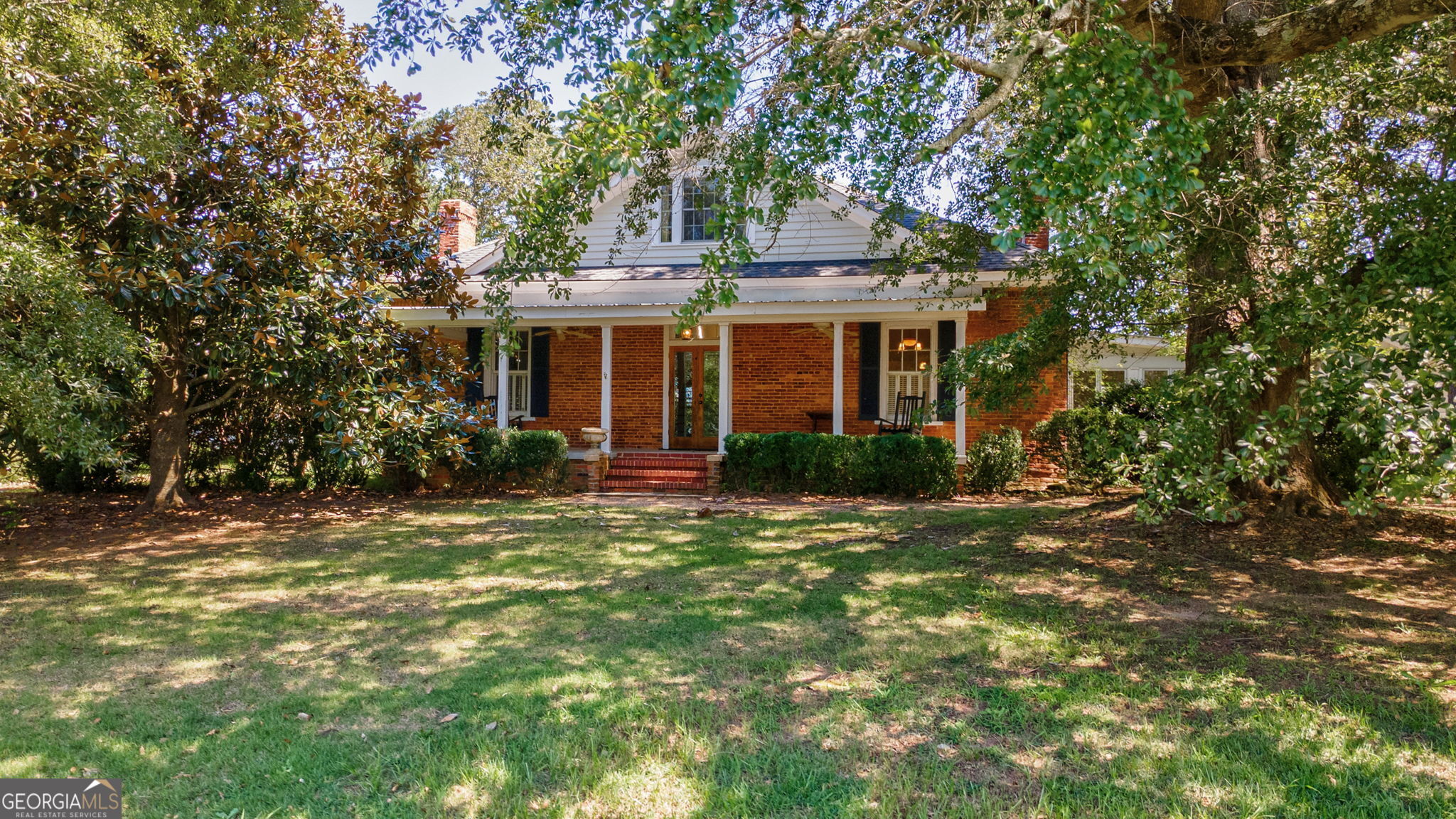 This charming, historic brick farmhouse, circa 1886, sits on 10 scenic acres with an additional 14.71 acres directly across the street. Pastoral beauty surrounds with a mature oak tree canopy, boxwoods and established pasture. A circle drive leads to the covered front porch with classic columns, welcoming you into a beautifully preserved home. Enter into a central foyer flanked by double parlors, each featuring gas fireplaces, original plaster walls, and elongated windows. The spacious formal dining room with fireplace is perfect for entertaining. A centrally located, updated kitchen includes a gas cooktop, double ovens, stainless steel refrigerator, granite countertops, and a fireplace. A large sunroom addition with tile floors offers serene views and natural light. Convenient full bath located near the kitchen and den. Cozy den with built-ins, fireplace, and access to both the rear patio and covered back porch. Laundry room with sink, adjacent to main-level, master bedroom. Large Master suite addition with walk-in closet, soaking tub, double sinks, and separate shower. One additional bedroom and full bath located on the second floor. Dairy Barn includes cement floor, electricity, and water-ideal for hobby farming or storage. Two-story, two-car detached garage with cement floor, electricity, separate bay, and floored upstairs. Open three-sided outbuilding with a tin roof, ideal for storing hay. Propane tank, electric water heater, two wells, septic tank. Land Features mature pecan, peach, crab apple, walnut trees and a fig bush, a small on-site cemetery. Property is in conservation, offering potential tax benefits and preserved rural charm. Only 15 minutes from downtown historic Madison, Ga square, 10 minutes to Lake Oconee and 25 minutes to UGA campus and Athens, GA.