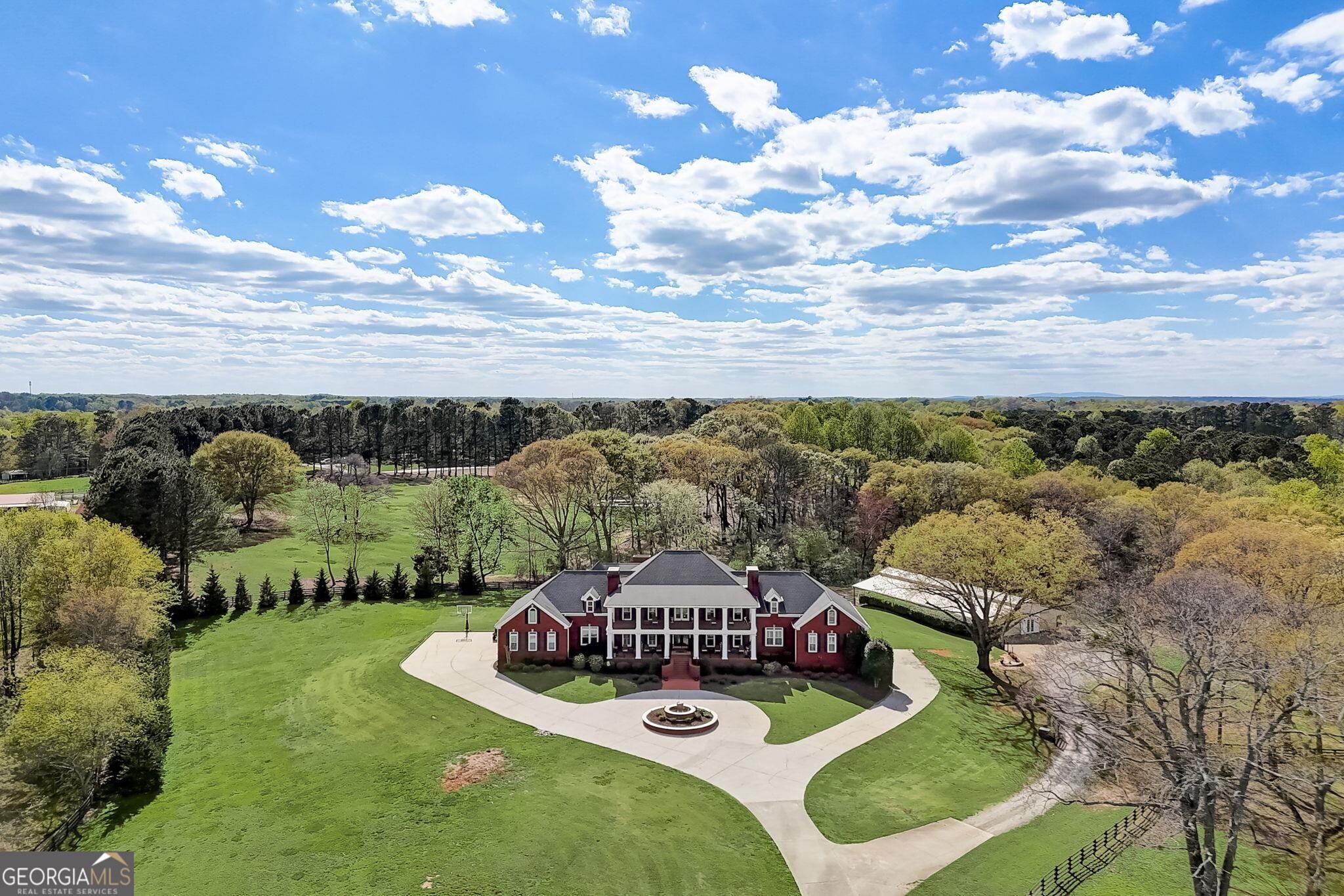 Experience luxury living at its finest with this unparalleled estate nestled in the heart of Forsyth County. Enter the estate through the private gates, drive along the beautiful driveway lined with Bradford Pear trees to the 15 meticulously manicured acres. This property stands as a testament to exquisite design and unparalleled craftsmanship. You'll be captivated by the charm of the four-sided brick Georgia Colonial home, boasting a majestic 50-foot front porch and balcony overlooking the scenic surroundings. A picturesque white gazebo graces the landscape by the stocked one-acre pond, offering a tranquil retreat for moments of reflection. For wine enthusiasts, the property features a small vineyard cultivating the historic Lomanto Grape, with a water drip system sourced from the pond. Stroll through fenced pastures and discover a 2100-square-foot barn, thoughtfully repurposed to host gatherings with friends and family, complete with a covered patio. Perfect for hosting events. For the Equestrian Lovers, stalls can be placed back into the barn. Upon entering the foyer, adorned with marble floors and a signature staircase, you'll be greeted by grandeur at every turn. From the formal living room with its dual chandeliers and fireplace to the expansive dining room and cozy study with wood coffered ceilings, every space exudes elegance and warmth. Exquisite custom crown moldings and trim truly add to the attention to every detail of this elegant home. The sunroom offers a casual retreat, perfect for family to gather, while the chef's kitchen is equipped with top-of-the-line appliances, cooking island with 6 burner gas cook top, subzero refrigerator, think granite counters, wall oven with warmer, even a fountain soda dispenser. Numerous cabinets and a large Butler's pantry with an additional refrigerator allows for plenty of storage. Large informal dining area for hosting large family dinners. Oversized laundry room with chute from upstairs. central vacuum. The main level boasts an impressive primary suite with a separate sitting room, fireplace, three walk in closets and luxurious en-suite bath with his and her vanities, freestanding tub, bidet and double shower and steam shower! There is a secondary bedroom with large walk in closet and its own private bathroom. Also on the main you will find a private office with a great view, 3 car garage equipped with hot and cold water and icemaker. Take the elevator or one of the 2 staircases to ascend to the upper level, where you'll discover 4 oversized bedrooms, each with walk-in closets and private bathrooms, along with two expansive bonus rooms and a loft area leading to a sprawling balcony. The terrace level is designed for entertainment, featuring a recreation area, built-in bar, billiard area, family room, and additional bedrooms and bathroom. A hidden concrete safe room provides added security and peace of mind. Outside, a heated saltwater pool and raised spa beckon for relaxation, while a pavilion offers a full outdoor kitchen, bar area, fireplace, and cabana bath for alfresco dining and entertainment. Fenced pastures, a stocked pond, the vineyard, the barn, apple, peach, crabapple trees and blueberry bushes these 15 acres offer pure pleasure. With an automatic commercial generator that runs on the natural gas, central vacuum system, and to your convenience. Countless other amenities, this estate truly stands as a one-of-a-kind masterpiece. Schedule your private showing today and discover the epitome of luxury living in Forsyth County.