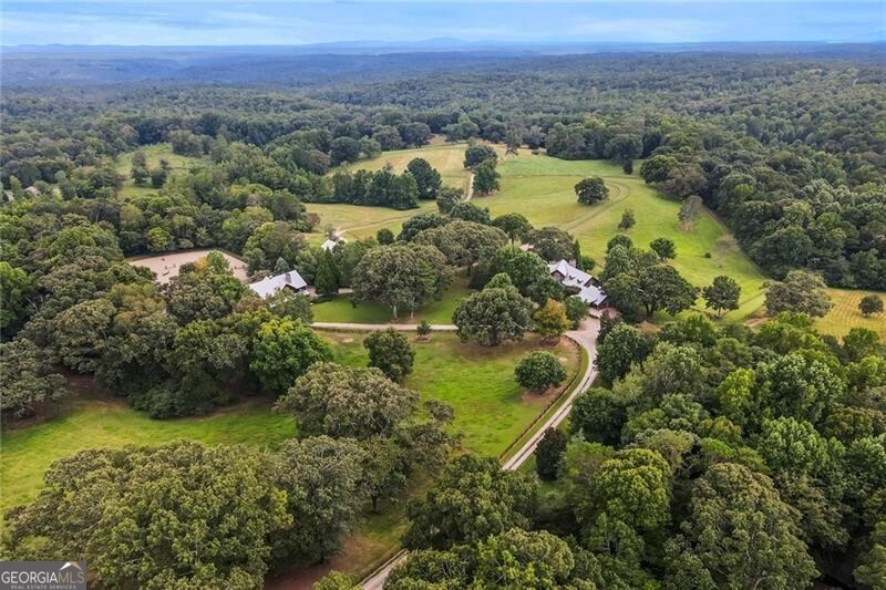 Experience absolute perfection on this 70 acre equestrian farm with rolling pastureland, three barns with 16 stalls, an incredible main house, a pool and a large guest house with elevator. Approached through a gated entry, the driveway winds past acres of fenced pastureland, beautiful hardwoods and riding arenas as you proceed to the wood and cedar-shingled main house. Evoking a bygone era, the home feels centuries old yet provides all the perks of modern living. Enter from the covered front porch into the enormous two-story grand hall with dining room, meant to feel like a log cabin with its wood-lined walls, wide-plank floors, exposed trusses and large stone fireplace. The adjacent gourmet kitchen provides all the luxuries for today's lifestyle with a large island, double-stacked cabinetry, stainless steel appliances, stone countertops, charming butler pantry and walk in pantry, a farmhouse sink and a nearby substantial laundry room. The kitchen flows seamlessly into the fireside keeping room and casual dining area. Huge double-hung windows wrap around the room and frame the sprawling views of the surrounding fields. French doors lead to the charming oversized screened porch with plenty of room for separate dining and sitting areas. Three en-suite bedrooms and large mud room complete the main level. Upstairs, you will find a large open office loft space, overlooking the grand hall as well as the primary bedroom featuring a cathedral ceiling with rustic beams, a fireplace, stained glass clerestory windows, a dressing room with two walk-in closets and an en suite bathroom with dual vanities, a jetted bathtub and a separate shower. Head downstairs to the incredible Garden & Gun-style terrace level, which features a wine cellar, fireside professional theatre room two built-in desks, a wet bar, a slate tiled game room, a gym or bedroom and a full bathroom. Venture outside to the refreshing, heated, saltwater pool with a large stone pool deck, a diving board and a motorized retractable pool cover. The property also features a four-stall barn with a tack room, a 12-stall barn with a washroom, and ample storage space. Spacious guest cottage above with elevator up is on the second level with a two-bedroom guest house with large additional office space. Perfect for a caretaker, this luxurious guest house includes an open floor plan with a two-story cathedral ceiling in the dining and living rooms, a white kitchen with an island, two large bedrooms, two bathrooms and a huge screened porch. Completely private and bordering a lake and creek with charming walking bridge, the property also includes an oversized arena, a round pen and a considerable outbuilding with a workshop and additional storage. Short ride by horse to Dawson Forest with endless trails (trail ride, mountain bike, hike). The property is also located close to a Elliot Field Private Airport, Atlanta Motorsports Park, Amicalola Falls, Lake Lanier and the North Georgia Outlets. A once-in-a-lifetime opportunity, this property is an equestrian lover's paradise!