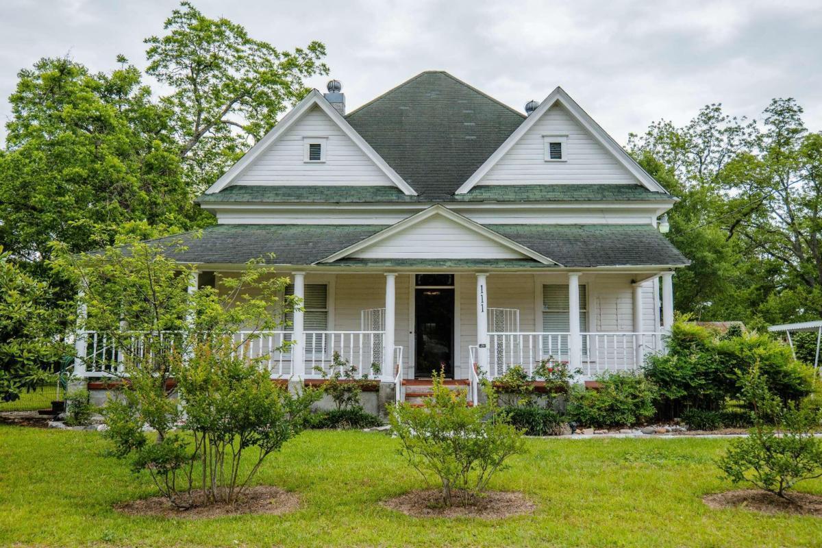 This 1891 American farmhouse offers charming character with added modern features, while preserving Victorian period beauty. From front yard, Walking past crepe myrtles, knock-out roses and magnolia, step from the large southern porch through the front door and into the open foyer of this gorgeous treasure. Featuring 15-foot ceilings, hardwood floors, and calming paint colors, this home is a breath of fresh, peaceful air. Inviting LivRm features wood-burning fireplace. Three bedrooms, each also have fireplaces with auxiliary LP heating available. At the end of the main hall, highlighted by the stained-glass window overhead, walk into the heart of the home where the family room/den awaits, featuring room for entertaining guests for parties or watching the big game, with built-in bar area. The 2021-remodeled kitchen features stainless steel appliances, red oak hdwd flooring, and Black pearl granite countertops. Dining Room is also open to kitchen and Den. Separate Laundry room is off kitchen/den. Large, full bath with jetted tub and separate shower is located off den as well. Step out onto screened porch/mudroom area and find storage/pantry room, and onto a sunny 12x16 deck, overlooking the lovely back yard featuring many fruit bushes and trees, including pecan, peach, figs, Bartlett pears, muscadines. Gaze over the 2+ acre, no-chemical pasture, perfect for growing organic crops, or grazing horses, cows, etc. Located in back of property is the red barn, with a loft, ready for hay or feed storage. Also in the yard is a utility shed/workshop with car shelter. Deep well, but city water available. 250-gal in-ground LP tank for aux heating. Add'l 1000 soft expandable attic space. **OPTIONAL purchase of additional .5 acre corner lot with rare 1950's 1250 s/f Mechanic's Workshop on it, built with aged cypress post and beams, 6k rated steel I-beam for heavy lifting, 4-6" concrete floors w svc pit and office space.** To see videos of property, text listing agent (Alicia Day)
