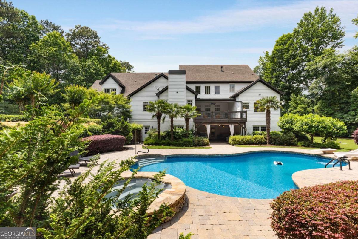 Welcome to your private resort-style sanctuary-an extraordinary retreat nestled on 3 lush acres in a quiet cul-de-sac with over 500 feet of peaceful lake frontage and a showstopping backyard oasis with a custom pool surrounded by lush landscaping and palm trees! This fully renovated masterpiece with 2 primary suites offers over 8,000 sq ft of elevated living, where luxury meets comfort and every detail is designed for relaxation, entertaining, and enjoying life to the fullest.Arrive via a brand-new winding driveway and step onto the inviting covered rocking chair front porch, where views of the manicured front lawn set the tone for the warm, welcoming lifestyle this home offers. Inside, you're greeted by a spacious, light-filled library with custom built-ins. Just beyond, a formal dining room easily seats 12-perfect for unforgettable entertaining. The vaulted living room with cozy fireplace flows into the heart of the home: an open-concept kitchen and keeping room with a second fireplace. The kitchen, completely updated in 2025, is a chef's dream with sleek quartz countertops, custom cabinetry, gas cooktop, double ovens, walk-in pantry, sunny breakfast area & breakfast bar-all open to the keeping room with fireplace. This space opens to a large deck with views of the stunning backyard. Around the corner, a beautifully designed utility wing includes a stylish drop zone and oversized laundry room with sink and ample storage.The main-level primary suite is a peaceful retreat with dual custom walk-in closets and a spa-like bath featuring new cabinetry, designer tile, deep soaking tub, and oversized shower-all overlooking the private pool. Upstairs offers 4 oversized bedrooms, 3 full baths, and 2 large hall walk-in closets for extra storage. Two bedrooms are en-suites; the others have private vanities. A second primary suite is set apart for privacy-ideal for a sitting area, office, or long-term guests, complete with en-suite bath and large walk-in closet.The terrace level is an entertainer's dream-featuring a home theater, spacious rec room, separate billiards room, and fully equipped second kitchen with bar and seating. A large workshop provides space for hobbies or storage. A 6th bedroom with walk-in closet and full bath is currently used as a fitness room and offers even more flexibility-perfect for multigenerational living. But the outdoor living space is the true showstopper. The terrace level opens to a covered patio that flows into a spectacular resort-style pool area. Surrounded by palm trees and lush landscaping, the heated gunite pool includes custom stone steps to a waterslide, built-in splash pad, and a stunning stone fireplace. A separate firepit area is perfect for evenings under the stars. The level backyard offers endless space for entertaining and play, with a batting cage and dedicated play area blending seamlessly into the grassy level private lawn. All of this overlooks 500+ feet of peaceful lake frontage with a private dock-ideal for fishing, kayaking, or launching a canoe. Great location - about 15 minutes from downtown Alpharetta / near Canton / schools / shopping Thoughtfully updated throughout with fresh interior & exterior paint, newer HVACs, 2 water heaters & designer finishes. This one-of-a-kind home offers luxury, space, privacy & a year-round resort lifestyle. Welcome to your forever home. Possible owner financing.