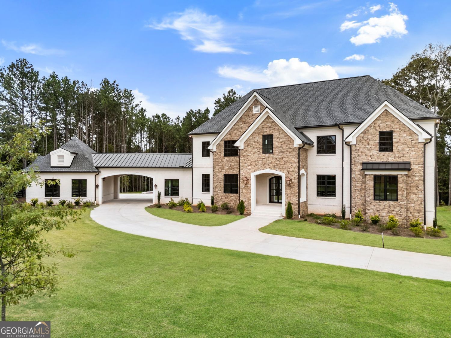 Thompson Manor delivers a rare combination of high design, privacy, and freedom-set on 1.63 acres in Milton with NO HOA. This property offers the flexibility to add a pool, pool house, or even expand the motor court, which already accommodates guests and collectors with ease. Step through dramatic iron and glass double doors into a home defined by soaring ceilings, bold architectural lines, and magazine-worthy design selections. The two-story living room makes a striking first impression with a sculptural curved staircase and walls of windows that flood the space with light. The chef's kitchen is both a showpiece and a workhorse, featuring custom European-style cabinetry, quartz backsplash, a waterfall-edge island, Thermador 48" range, and paneled refrigeration. The space flows effortlessly into the dining area and grand room, where a floor-to-ceiling Quartz linear fireplace, wood-beamed ceiling, and built-in wet bar elevate entertaining. Folding glass doors extend living outdoors to the covered porch with its own fireplace and grill connections. The main-level owner's suite is a private sanctuary, opening to the porch and featuring a spa-inspired bath with dual rainhead showers, floating vanities, illuminated mirrors, a freestanding soaking tub, and luxe marble finishes. A custom dressing room with integrated laundry adds both style and function. Upstairs, three en-suite bedrooms include two with private balconies. A bonus room offers flexibility as a fourth suite, while a secondary laundry with custom built-ins keeps everything organized. Additional features include wide-plank hardwoods, a walk-in pantry, mudroom with custom storage, EV-ready three-car garage with epoxy floors and pet wash station, and a porte-cochere for dramatic curb appeal. The detached garage has room for a car lift. The unfinished terrace level provides room to grow with space for a gym, theater, or guest suite. Located in one of Milton's most desirable areas-with award-winning schools and close proximity to Crabapple, Alpharetta, Avalon, and GA-400-this home delivers a refined lifestyle without the restrictions of an HOA.