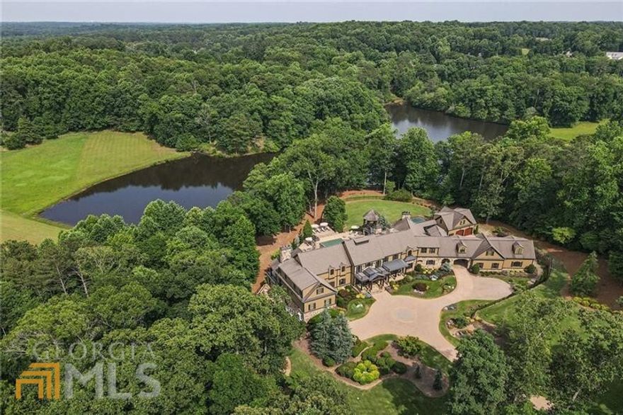 Situated on 5+/- acres on prestigious Dorris Road, privacy and tranquility await at this spectacular gated lakefront estate in the heart of Milton. A long driveway creates a dramatic approach to this sprawling home prefaced by a motor court with flanking parking areas. A porte coch re leads to the home's private six-car garage featuring two car lifts. The stone-lined covered front porch invites with a daybed swing and space for rocking chairs, the perfect setting for relaxing.  Enter the home through double front doors into the grand foyer where stone floors, rich woodwork and a gracefully curved central open staircase impress. Inviting living areas with 12-foot ceilings, solid mahogany doors and oversized mantels create grand yet intimate entertaining spaces. Enjoy numerous French doors opening to the expansive rear deck from many main-level living rooms, all with stunning lake views. Pristine hardwood floors flow throughout and create a cohesive flow between rooms.  The stunning kitchen features a sizeable, tiered island with seating and granite double ogee-edge countertops, a copper farmhouse sink, furniture-style cabinetry, a Wolf gas range with a griddle and a double oven, a pot filler and a hidden scullery. The kitchen flows seamlessly into the casual dining area and the vaulted keeping room, with a floor-to-ceiling stacked stone fireplace.   Sliding French doors provide easy access to the outdoor grilling station, fireside sitting area and covered pavilion. Supported by a colonnade of stone arches, the  rear deck creates a large, shaded covered terrace below with a summer kitchen, dining and sitting areas and a second grilling station with a beverage center. The refreshing pool offers a generously sized shallow end, two tanning shelves, a deep end and a spa. This fully fenced resort-style backyard includes a full-size sports court, an expansive grassy play area, professional landscaping and immense privacy.   Venture back inside the home to discover the serene main-level primary suite. This retreat commences with an entry foyer opening to the spacious bedroom and adjacent sitting area lined with windows on three sides. A stately fireplace punctuates a wall of built-ins, and there is a tucked-away morning bar. A second fireplace and a dry sauna are luxurious additions to the en suite bathroom. Separate vanities offer abundant storage, and a private deck serves as a peaceful escape.  The upper level boasts 10-foot ceilings, a second primary suite and luxurious en suite bedrooms, each with the same level of finishes and a second laundry room. The living spaces continue on the terrace level, which includes a gym with two showers, a billiard room, a state-of-the-art media room, a stunning wine cellar with a tasting room, a large craft room and a quiet guest suite. A convenient elevator provides access to all three levels.   Additional noteworthy features include a two-story wood-lined study on the main level, eight fireplaces, a 26-camera security system, a one-bedroom, one-bathroom carriage house, a new Control4 home automation system, as well as numerous other upgrades throughout all three levels and the grounds. Located near excellent schools (Award winning Milton High District & near a sought after private school). Approximately two minutes to downtown Milton and 10 minutes from downtown Alpharetta, Avalon and GA-400, this home offers privacy and convenience. Welcome home to this exceptional gated estate in Milton