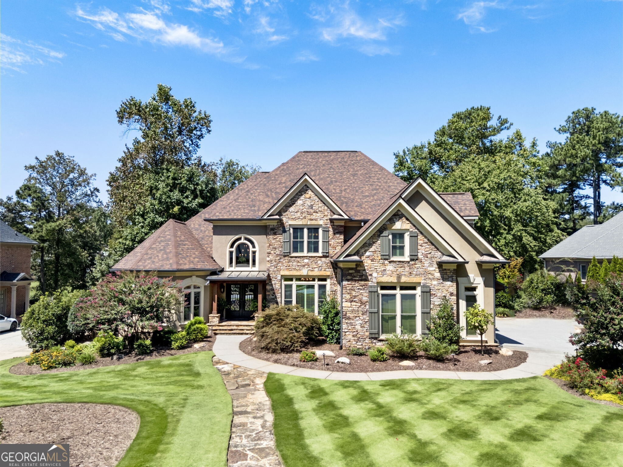 Tucked away in a quiet cul-de-sac within Hamilton Mill's vibrant golf course community, this elegant estate offers timeless style, thoughtful design, and resort-style outdoor living. Perfectly positioned along the seventh hole, the home showcases sweeping fairway views and a beautifully landscaped half-acre lot with a private pool. Upon entering, you are greeted by a bright two-story foyer that sets the tone for the main level. To the right, the formal dining room seamlessly transitions into a custom coffee bar, leading into the spacious kitchen-perfectly crafted for casual living and entertaining. On the left side of the foyer, a private office offers a delightful front-facing view of the yard, providing a serene workspace. Further down the hall, the formal living room impresses with floor-to-ceiling windows, a striking fireplace, and built-in bookcases on either side, creating an inviting space for gatherings. Past the living room is the kitchen and family room. The stylish and functional kitchen features stainless steel appliances, bar seating at the large island, newly painted cabinets, a walk-in pantry, and a sunny breakfast area that opens into the family room. The family room is adorned with a stone fireplace, generous seating space, and access to the back porch. This area acts as the center of the home. The primary suite on the main level serves as a luxurious retreat, featuring an updated spa-style bathroom. It's equipped with a sleek glass-enclosed shower, modern vanities, and a stunning stained-glass window that brings a touch of elegance and charm. Upstairs, you'll find three spacious secondary bedrooms. Two of the bedrooms share a Jack-and-Jill-style bathroom, each with its own separate vanity and ample closet space-making them ideal for family members or guests. The terrace level of this home is a beautifully finished extension of the main living space, designed with versatility and entertainment in mind. At the center of the terrace level is a fully equipped second kitchen; great for hosting gatherings or preparing poolside meals. This kitchen features custom cabinets, black appliances, and a large open area that flows into the main living area. A spacious media room offers space for billiards, table games, and a seating area. The wonderful home theater features tiered seating, built-in surround sound, and dimmable lighting. In addition to entertaining areas, the terrace level includes a guest suite or flex room and a full bathroom. French doors lead directly out to the covered lower patio, where seating areas and under-decking provide shade and comfort while enjoying views of the pool and golf course, as well as access to the gas grill. The backyard of this exceptional home is a private retreat, perfect for both relaxing and entertaining. At its center is a stunning gunite pool, surrounded by lush landscaping and a raised hot tub with a cascading waterfall for a resort-like feel. Just beyond, a built-in fire pit and spacious patio with seating create ideal spots for gathering, dining, or enjoying peaceful golf course views. This home combines quality craftsmanship, a bright and spacious layout, and hardwoods throughout. With modern updates, a fully finished terrace level, and a backyard built for entertaining, this home is the perfect combination of luxury finishes and comfort.