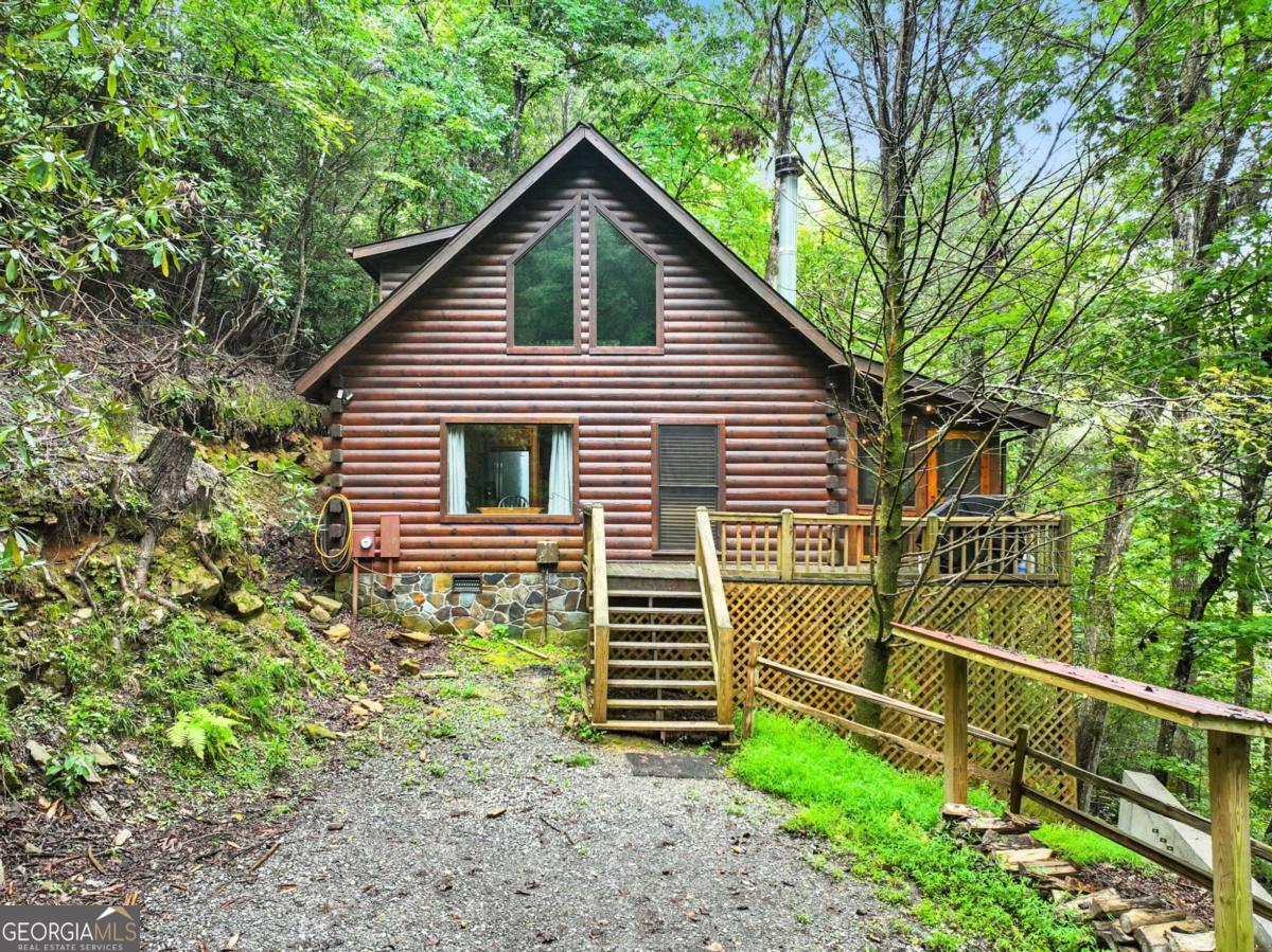 Your riverfront retreat awaits with this inviting 3-bedroom, 2-bath cabin perched on the Ellijay River, offering the ideal blend of tranquility, recreation, and convenience. Whether you're seeking a private mountain escape, a full-time residence, or a proven turnkey rental, this home is ready to deliver. Step inside this true log cabin to find a warm and inviting interior featuring a floor-to-ceiling stone wood-burning fireplace in the cozy living area. The rustic kitchen stainless steel appliances with a beautiful hammered metal farmhouse sink and dining space next to a large picture window. The main floor has two bedrooms, one overlooking the river, and a full bath with custom vessel sink, and a laundry closet. The upstairs loft has a king bed, cozy nook, its own arcade gaming system that is fun for all ages, plus a beautiful bathroom with tiled shower. Outdoor living is where this property truly shines. Sip morning coffee on the screened porch, soak in the hot tub under the stars, or unwind by the private fire pit right at the river's edge. Head down the steps to the riverfront dock that offers excellent fishing or the perfect spot for simply listening to the soothing sounds of flowing water. Nestled in a charming community that greets you with a quaint covered bridge, the cabin feels worlds away, yet you're just minutes from hiking in the Chattahoochee National Forest, apple orchards, wineries, and the boutique shops and variety of dining found in Historic Downtown Ellijay and Blue Ridge. This cabin comes fully furnished and turnkey making it move-in or rental ready from day one. Your riverfront retreat awaits!