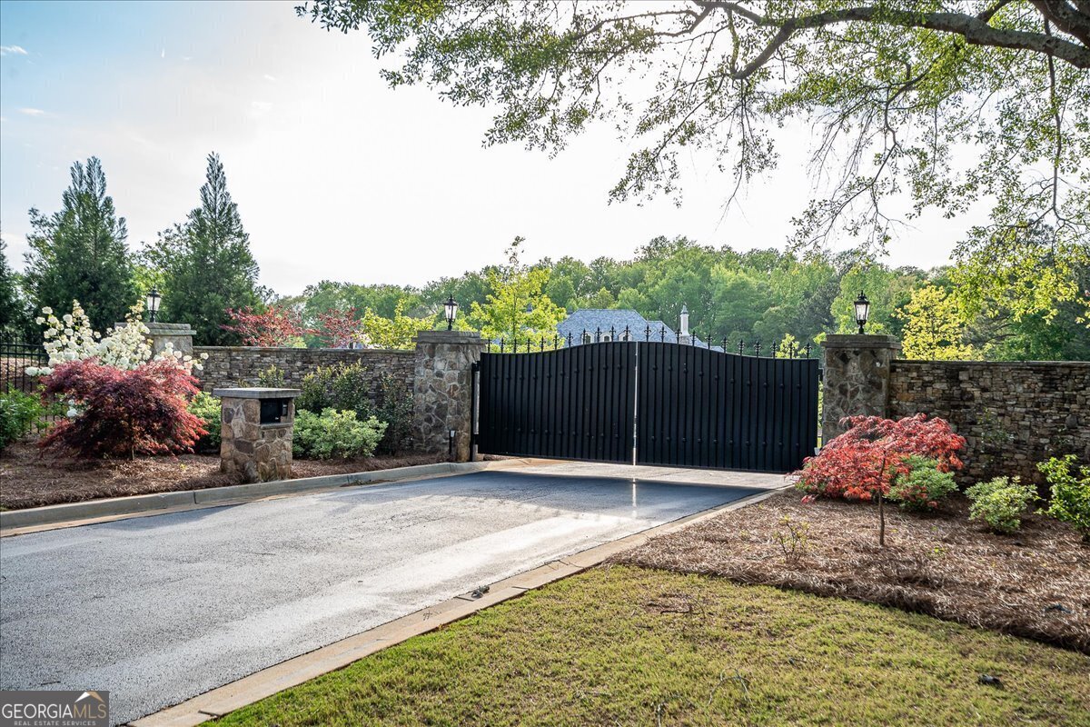 LUXURY ESTATE ON 10 ACRES! This custom-built home offers unparalleled grandeur and sophistication with a private gate. As you enter the home, you are greeted with a magnificent foyer boasting an impressive iron railing and banister. To the right of the foyer lies a handsome two-story library/office adorned with meticulously crafted wood-paneled walls, providing an inspiring space for work or relaxation. The center of the home is the exquisite living room, featuring a majestic fireplace and wet bar, perfect for entertaining guests in style. Adjacent to the living room is the stately dining room with a fireplace, where memorable gatherings are sure to take place. The chef's dream kitchen leaves nothing to be desired, equipped with four ovens, two dishwashers, two warming drawers, 48" Wolf gas range, sub-zero refrigerator, and a walk-in pantry for meal preparation. The room adjacent to the kitchen is the perfect area for a wine room as the beautifully crafted iron door suggests. Opening from the kitchen is a palatial great room with soaring eighteen-foot ceilings, seamlessly blending with a breakfast area, ideal for casual dining. The master suite is a sanctuary unto itself, featuring a lovely sitting room, separate his and her closets, with one closet boasting two stories of custom detailed storage including glass cabinets with lights. The master bathroom is a haven of luxury, complete with a gas fireplace, oversized tub and steam shower. For your convenience a home gym with a sauna is located between the master bathroom and library. One of the wonderful designs of this estate is that all of the main living spaces on the back of the home have glass French doors leading to an expansive screened porch. Ascending the lovely staircase, a circular balcony overlooks the foyer, granting access to all areas of the upper level. Five spacious bedrooms, each with en suite bathrooms offering comfort and privacy for family and guests. Also on the second floor there is a media room, game room with wet bar, and a sizable office that caters to various recreational and professional pursuits. There is a shaft ready to be finished for a future elevator for easier access to the upper floor. The garage not only includes a workshop/craft area, but also offers 5 separate heated and cooled parking spaces. Inside the garage there are stairs that lead to the area above the garage where you will find a potential in-law suite. Outdoor living is elevated with a vast screened porch featuring radiant ceiling heaters, a commercial pizza brick oven, and two glass fireplaces overlooking the saltwater pool, surrounded by meticulously landscaped grounds. In every detail, this estate epitomizes luxurious living, offering a harmonious blend of sophistication, comfort, and unparalleled amenities for the most discerning homeowner. The location of this haven cannot be beat with its proximity to UGA, Athens, quality healthcare, cultural arts and the award-winning school district of Oconee County. Several photos have been digitally altered (paint colors and removal of drapes).