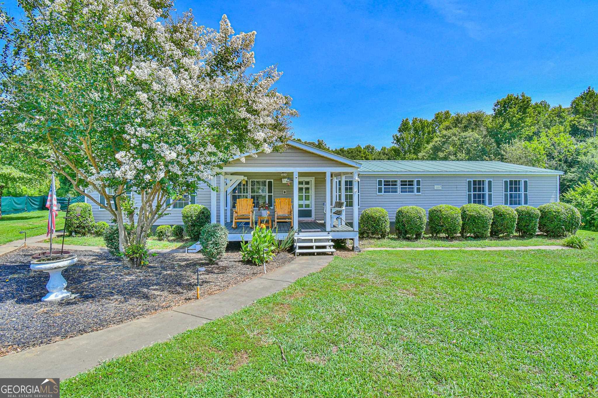 GRAB YOUR TOOTHBRUSH & CLOTHES. Welcome to your own private oasis! This extraordinary listing presents an awesome Fleetwood Manufactured home COMPLETELY FURNISHED with permanent foundation and situated on an expansive 8.22 acre lot, providing the perfect blend of comfort, space and tranquility. The front 4+ acres is grassed and the back acreage is wooded perfect for deer hunting with deer stand in place or deer watching. Nestled in the heart of nature, the property offers an ideal retreat for those seeking a serene lifestyle. The home is in pristine condition and boasts an incredibly spacious interior with generous living area and plenty of room for everyone to spread out and relax. The master bedroom is a true retreat with an en-suite bathroom with soaking tub, separate shower and plenty of closet space. Both of the secondary bedrooms are big enough for king sized beds. The island kitchen is not lacking for counterspace or cabinets and the refrigerator, washer & dryer and countertop microwave stay with the home. There are 2 Storage buildings on the property; the larger one that is 10’ X 12’ actually has power. The smaller one which is 8’ X 10’ and the green house stay with the property as well. There is a 20’ X 20’ Carport and the most unique hunting stand or play house which is 12’ X 10’ Covered and built with post 5 feet off the ground. Outside, the large yard provides plenty of space for kids and pets to play, while the surrounding woods provide privacy and a sense of tranquility. Imagine spending your evenings on the covered back porch or sitting on the front porch and watching the sunset. Trusted Lender - Casey Simmons 706.968.8709, NMLS# 2303959, with Homeowners Financial Group